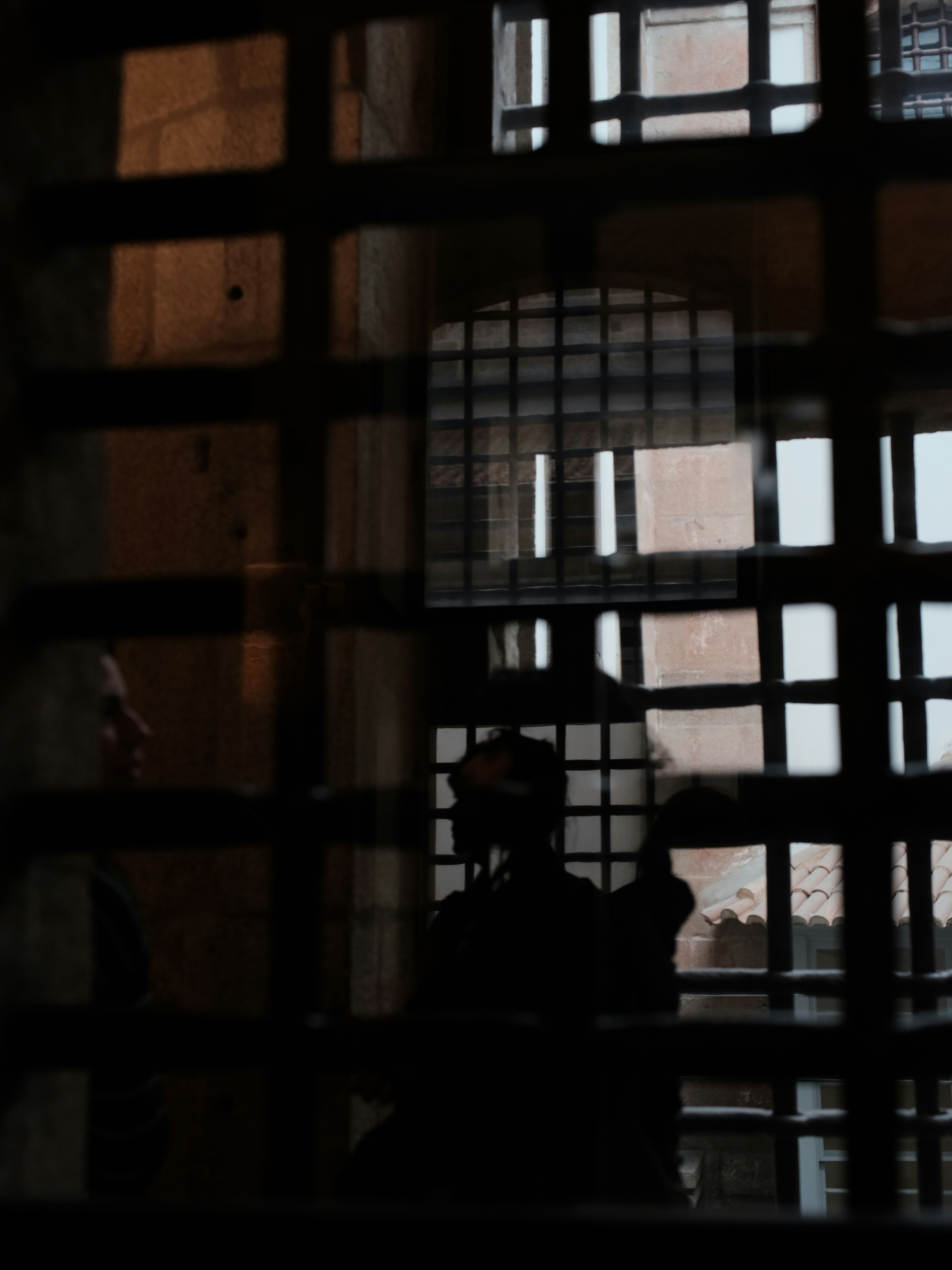 Two figures seen through prison bars in dim light.