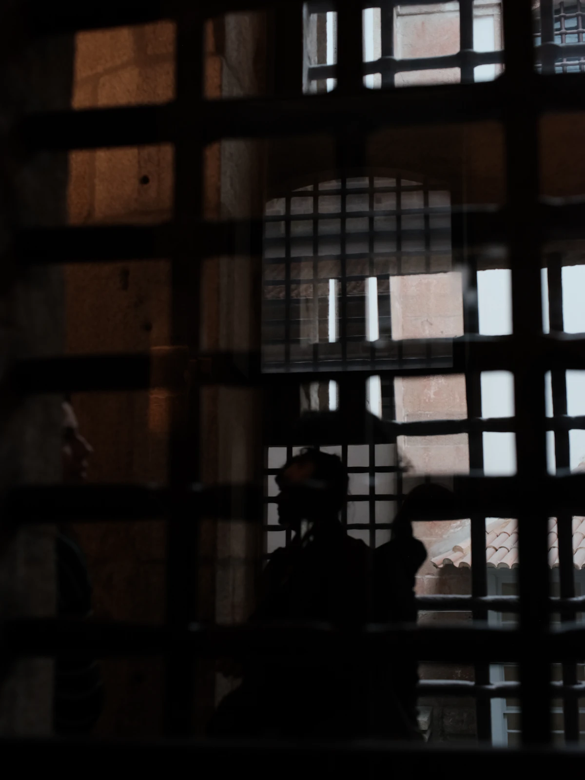 Two figures glimpsed through prison bars in dim light