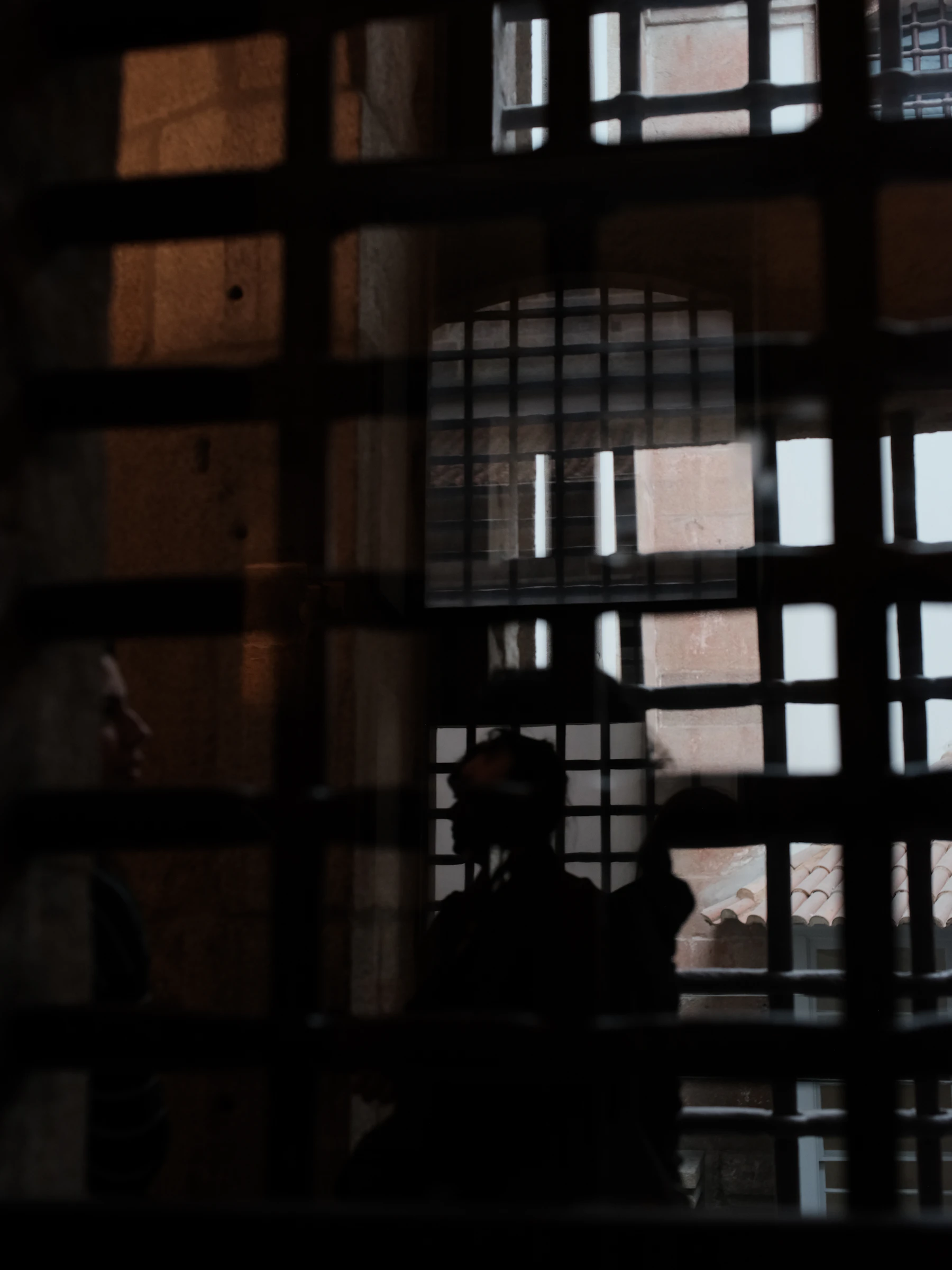 Two Figures Seen Through Prison Bars In Dim Light