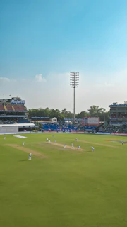 Cricket match in progress on a sunny day at stadium.