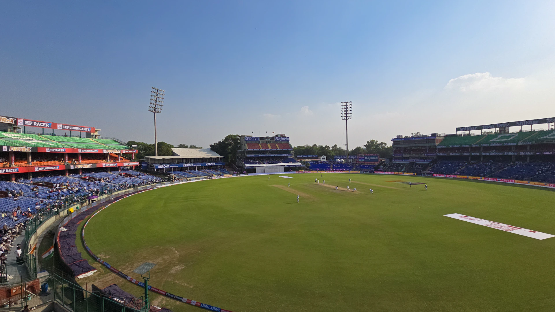 Cricket stadium with green field and blue sky.