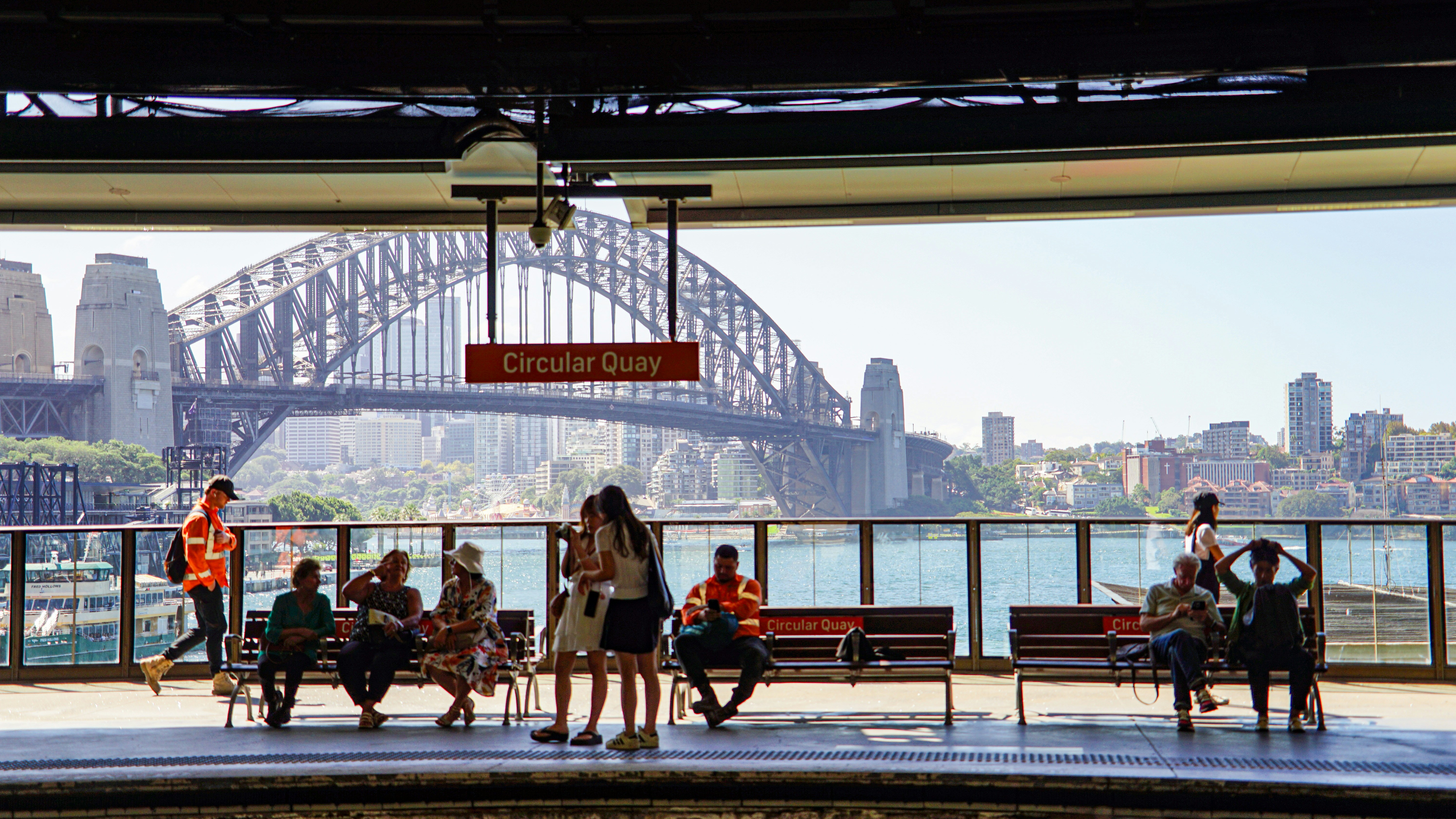 People wait on a platform with sydney harbour bridge background.