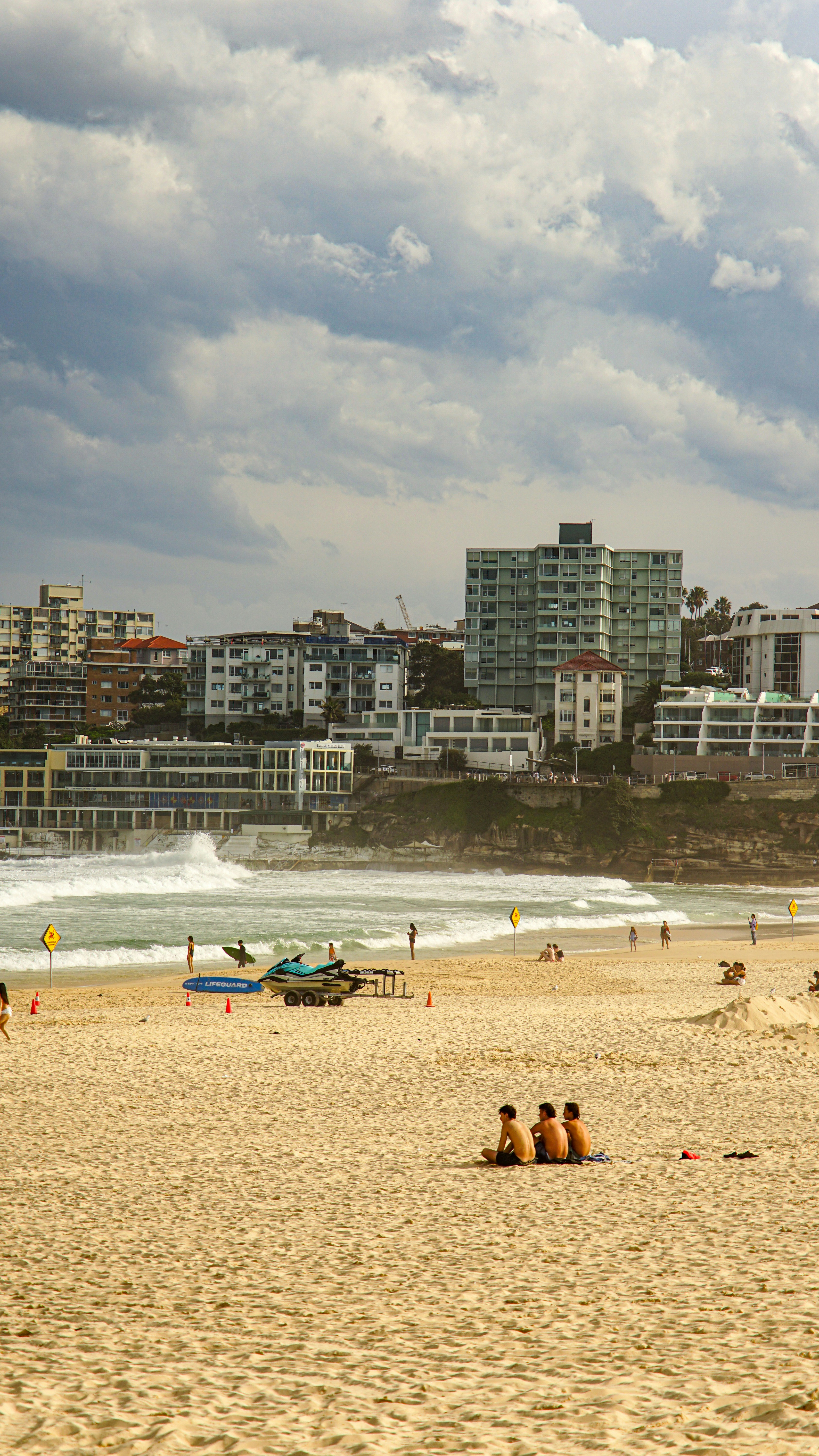 People sitting on a sandy beach with city buildings behind.