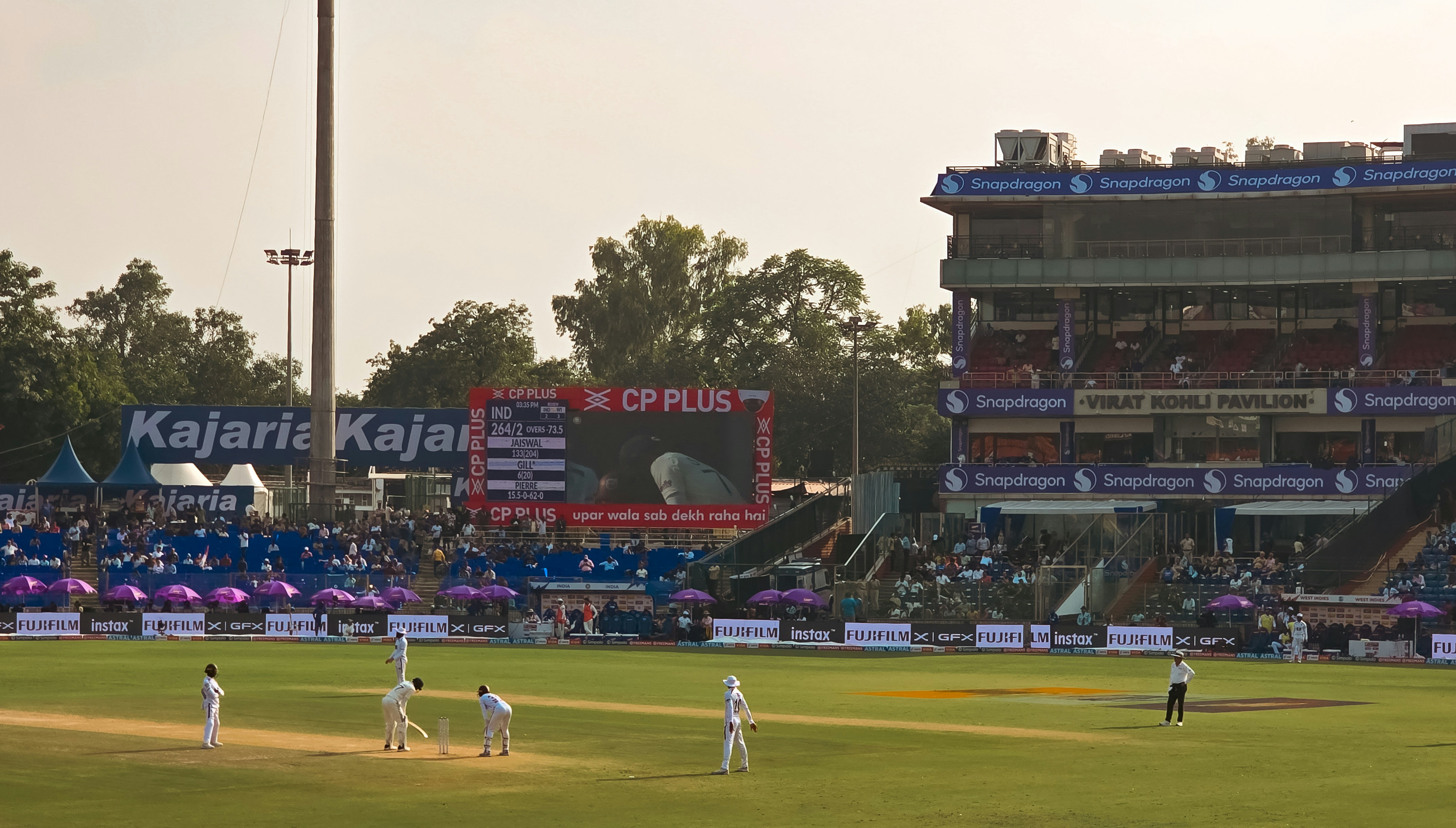 Cricket match in progress at a stadium with spectators.