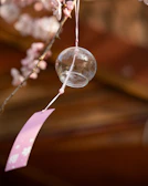 A glass wind chime hangs from a cherry blossom branch.