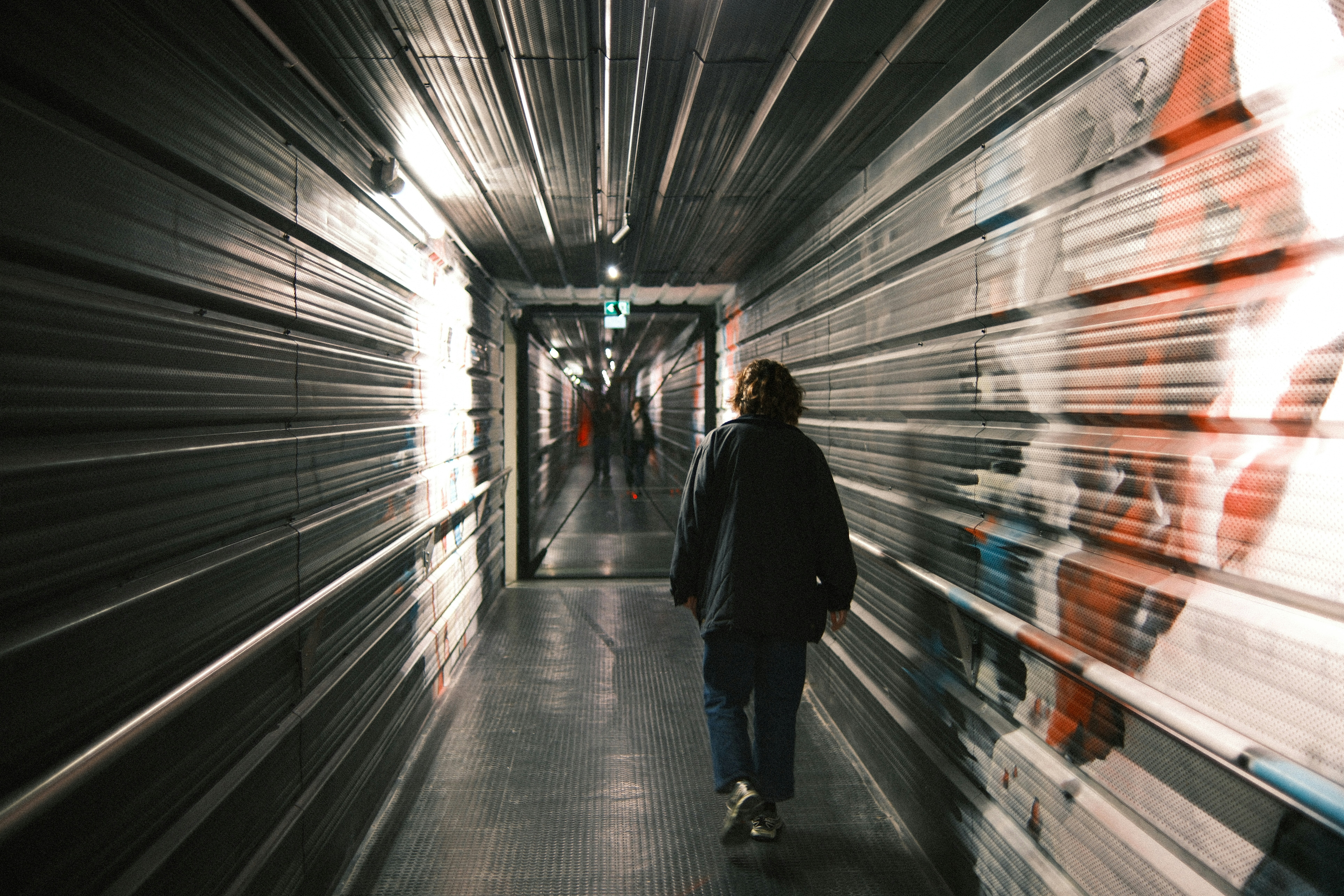 Person walks down a long, dark, industrial hallway.