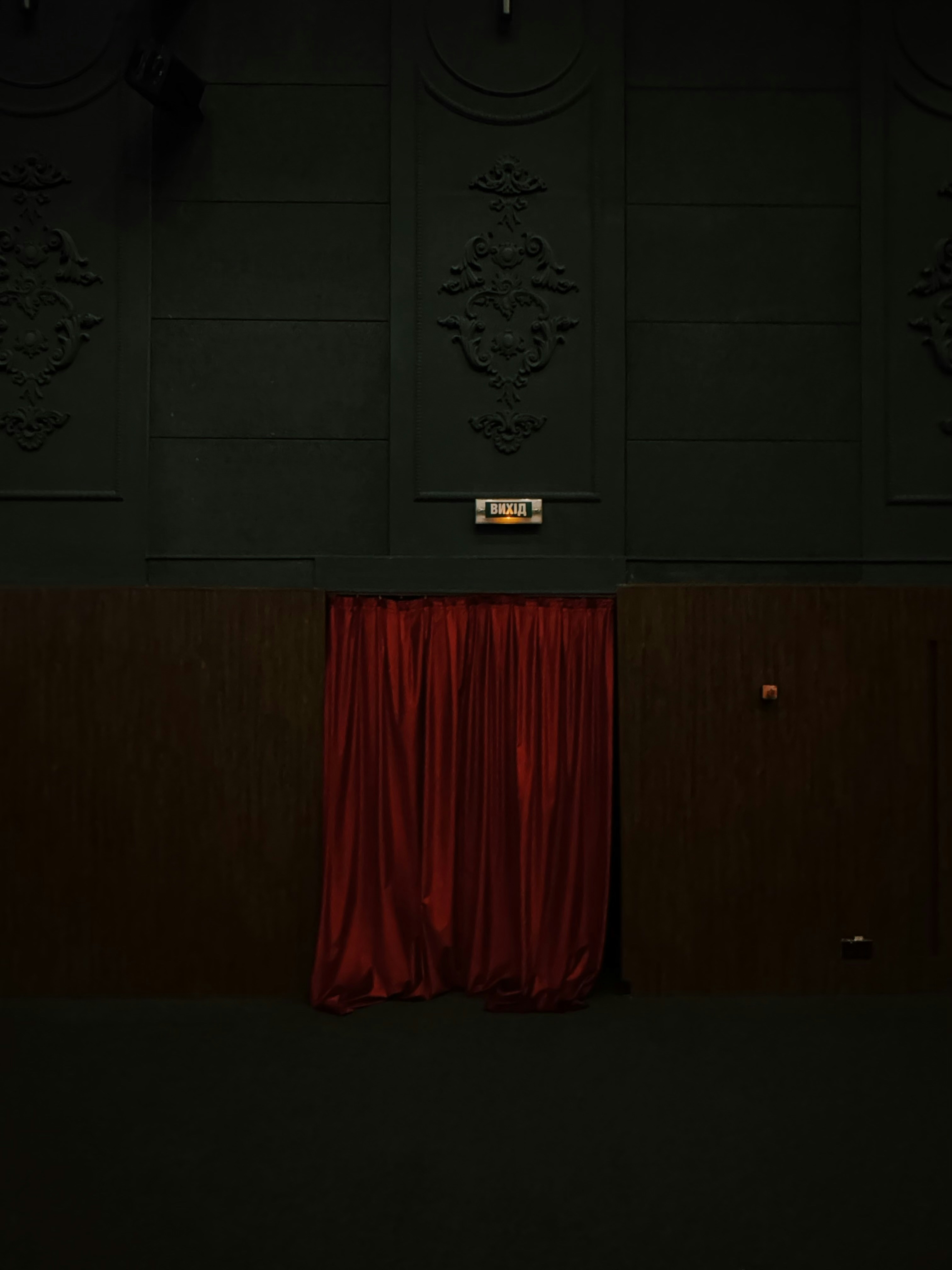 Red curtains hang in a dark, ornate room.