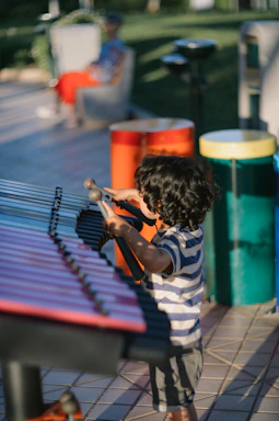 Child playing xylophone outdoors with colorful drums behind