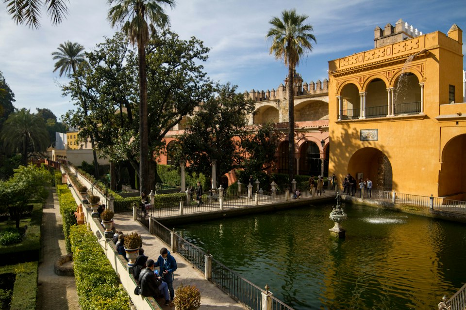 An ornate Moorish palace courtyard with a long reflecting pool at the Real Alcázar
