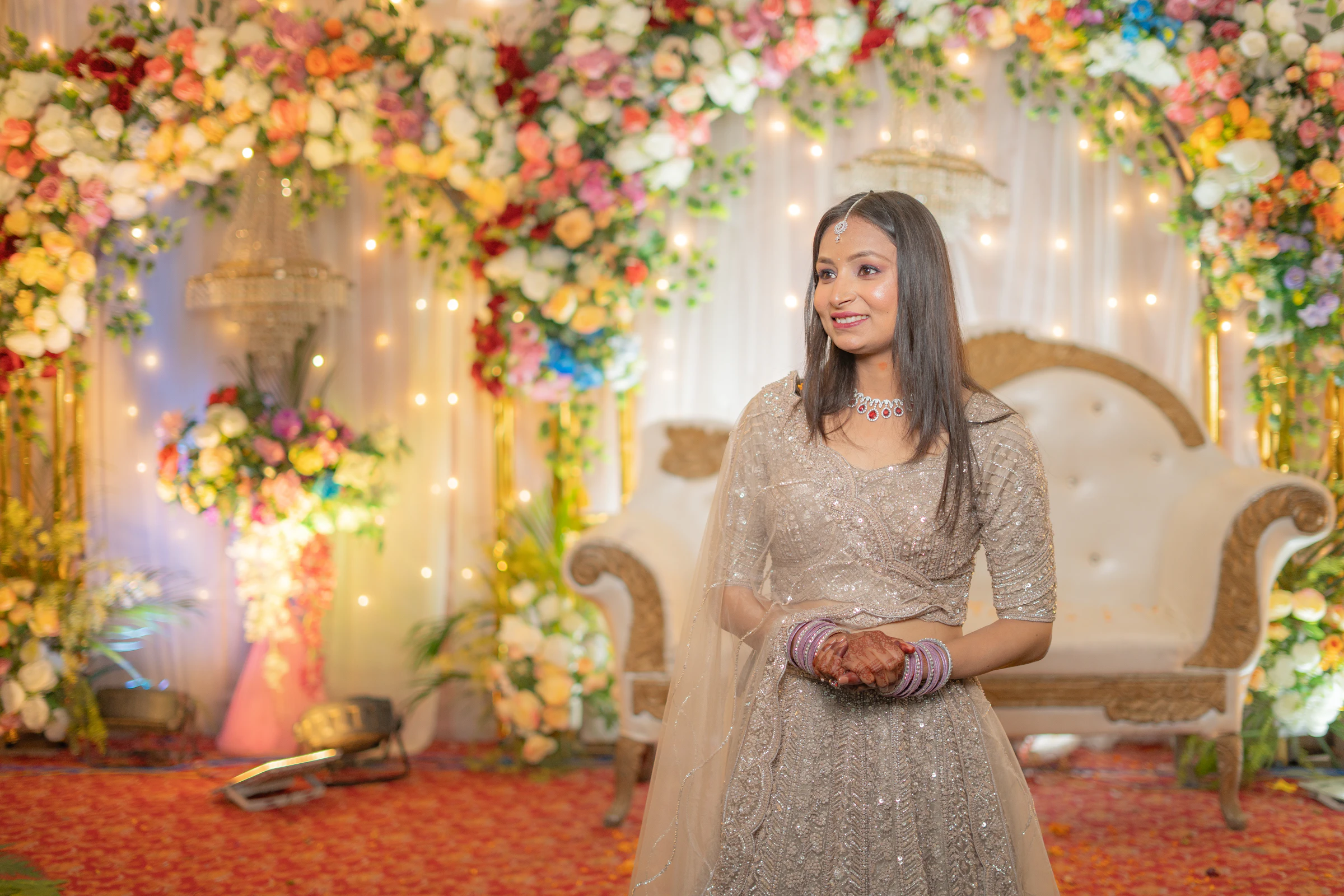 A woman in a sequinned silver lehenga on a flower-decorated wedding stage