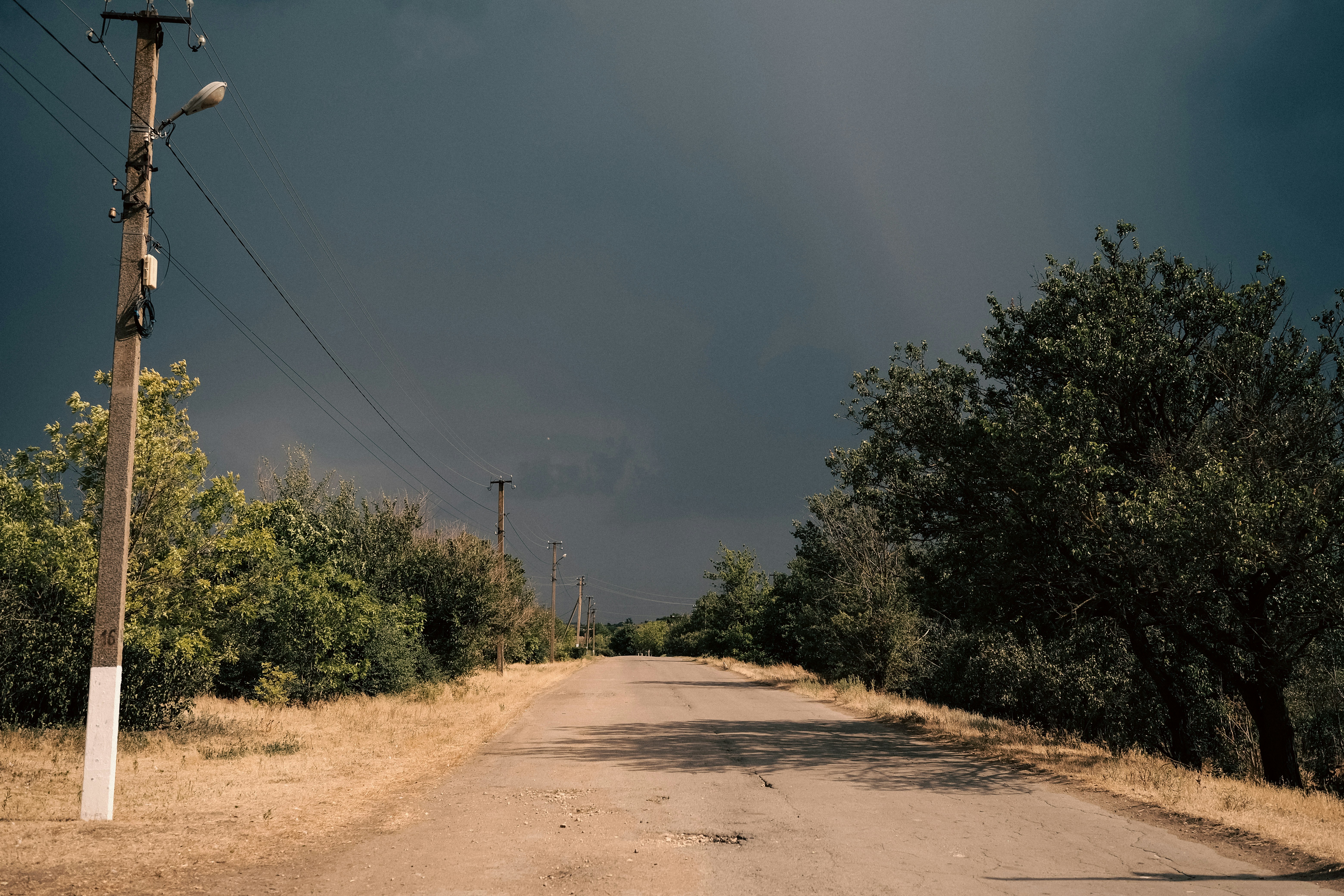 A dirt road leads towards a dark, stormy sky.