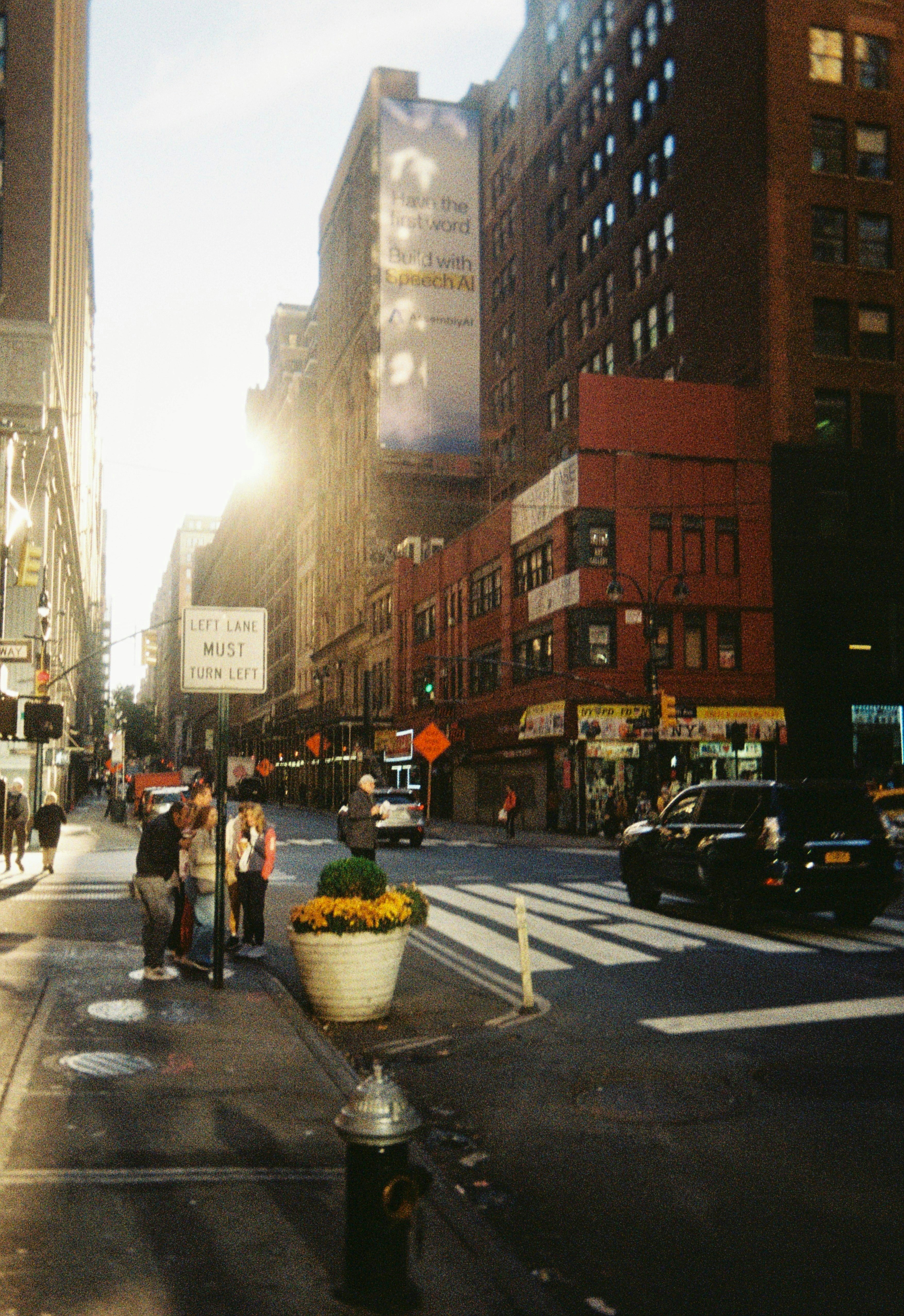 La luz del sol se cuela por una calle de la ciudad con edificios y coches.