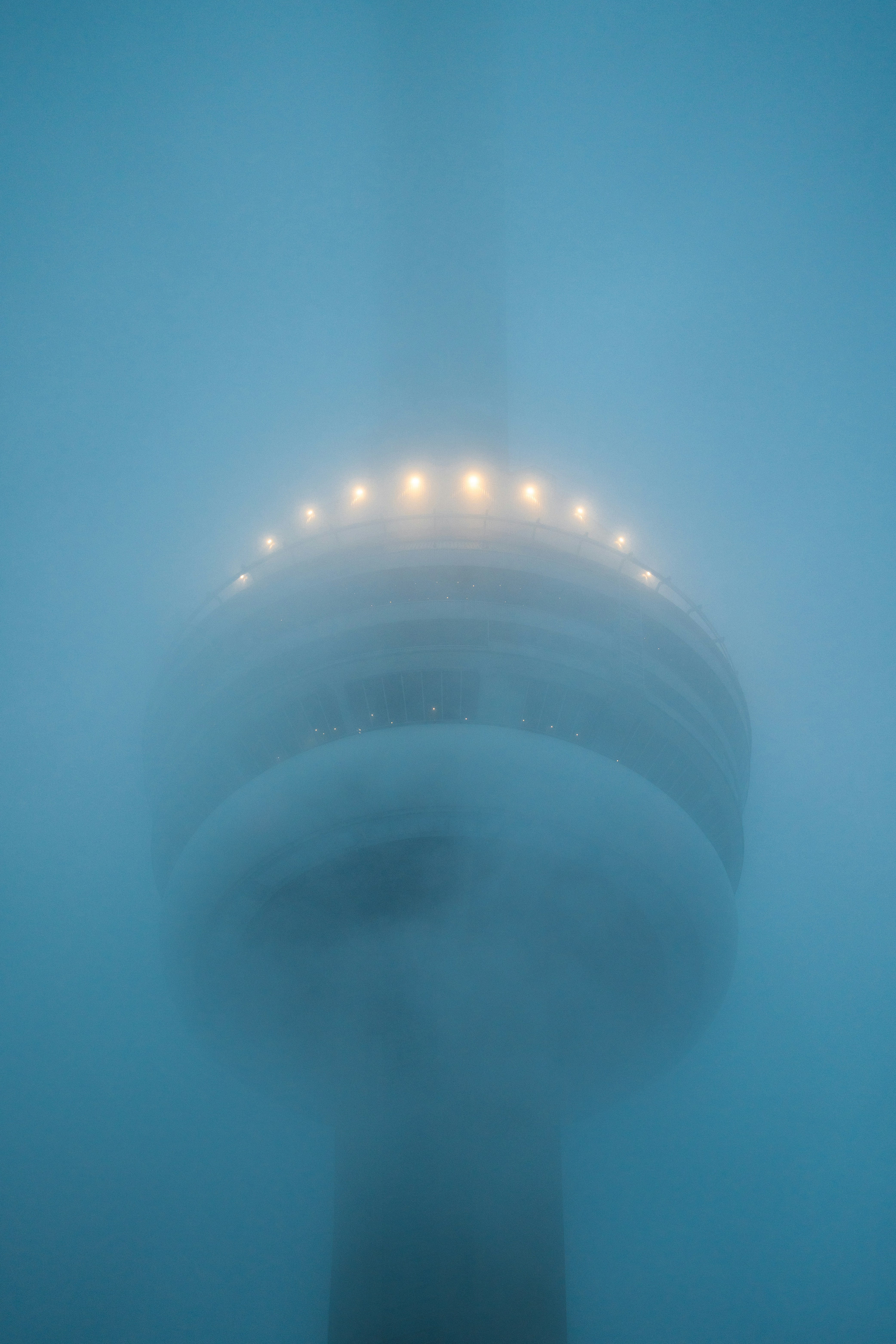 A tall tower emerges from thick fog at night.