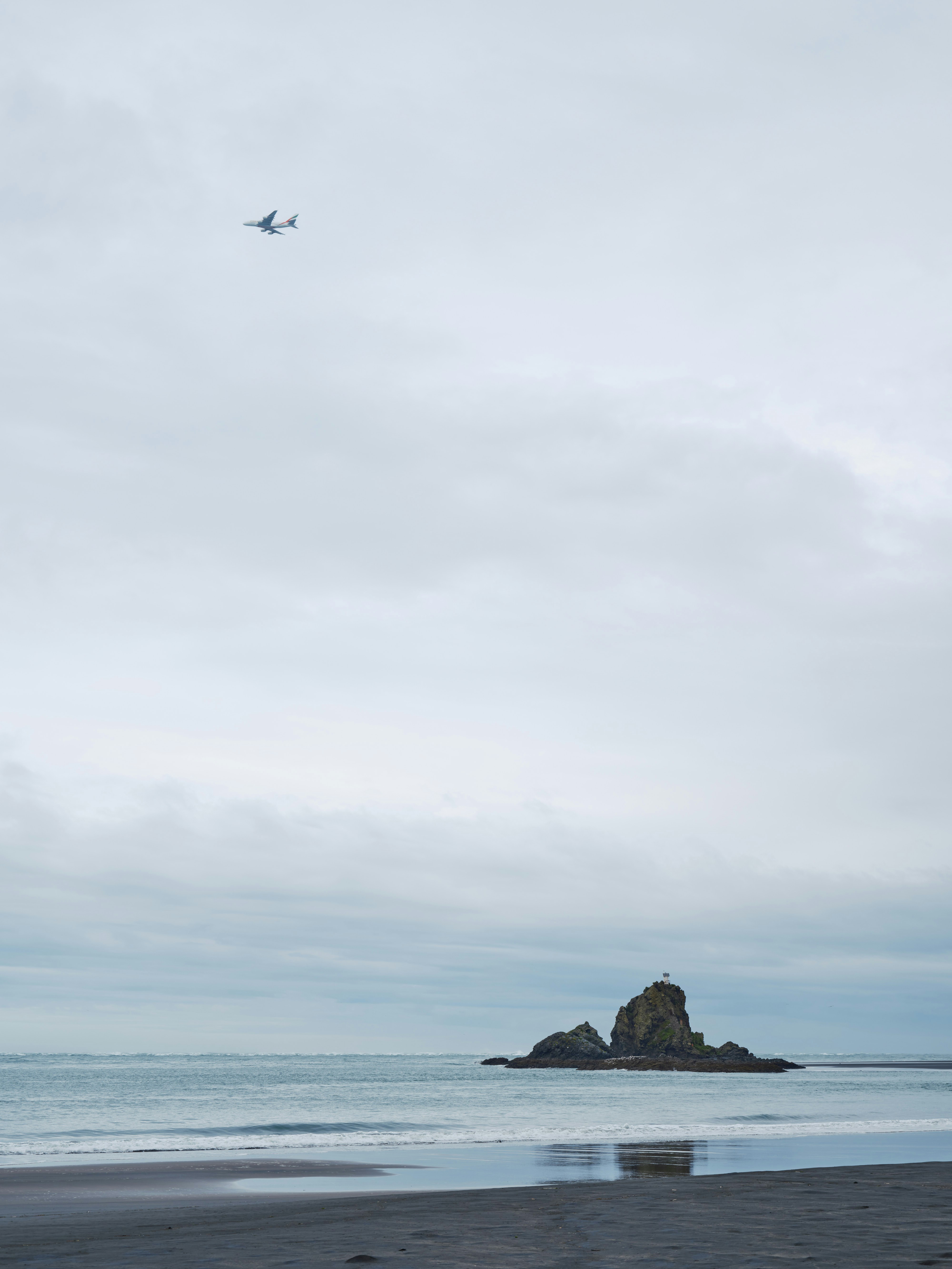 Airplane flies over a rocky island near a beach.