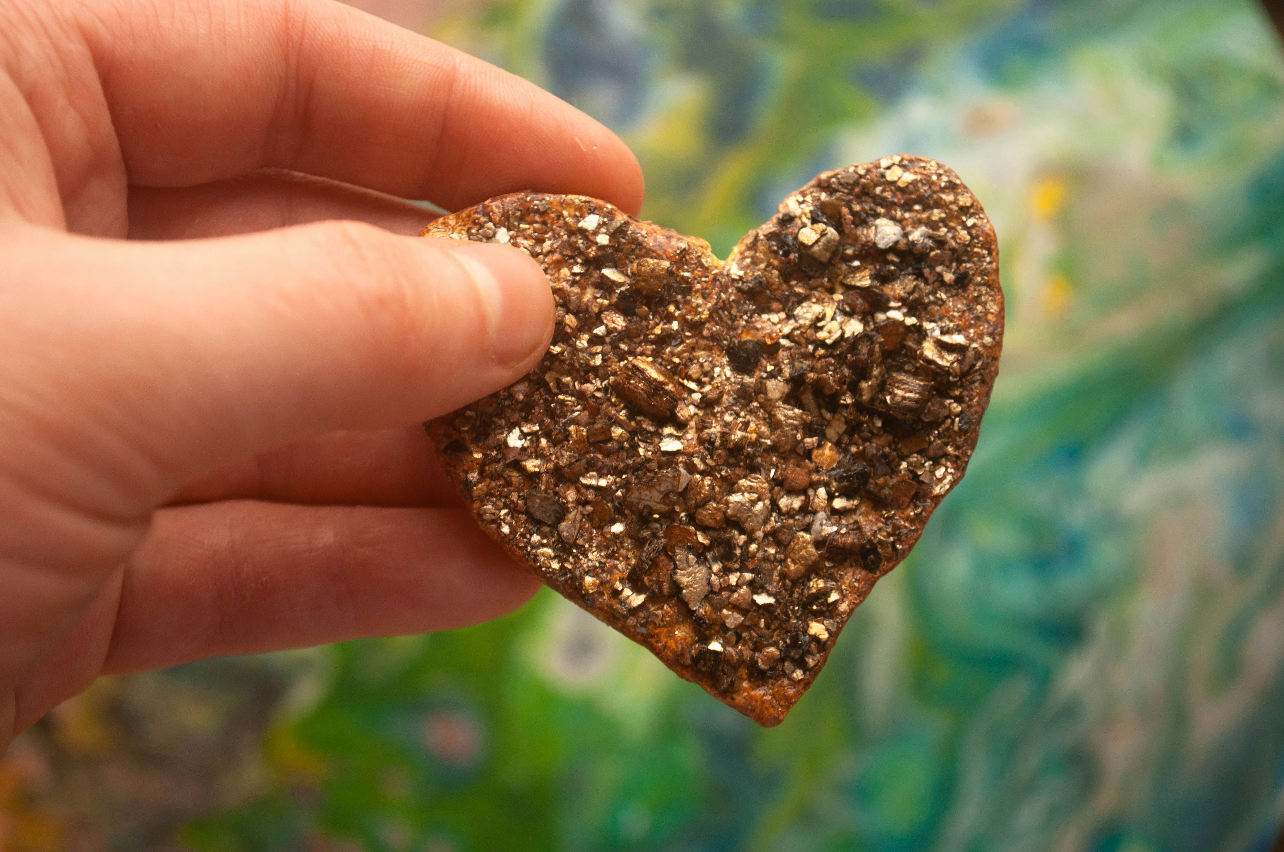 Hand holding a heart-shaped object with sparkling texture.