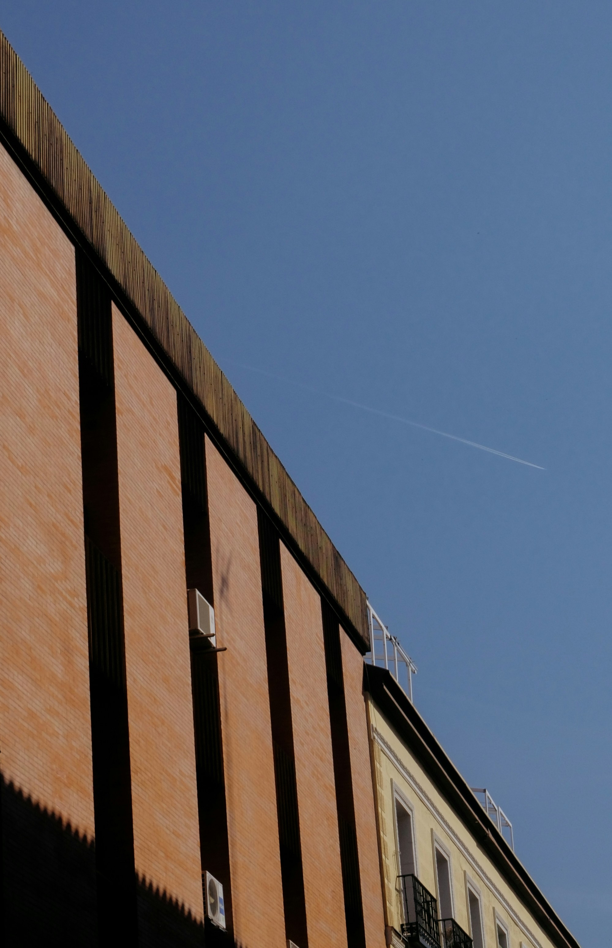 Building facade against a clear blue sky with airplane trail