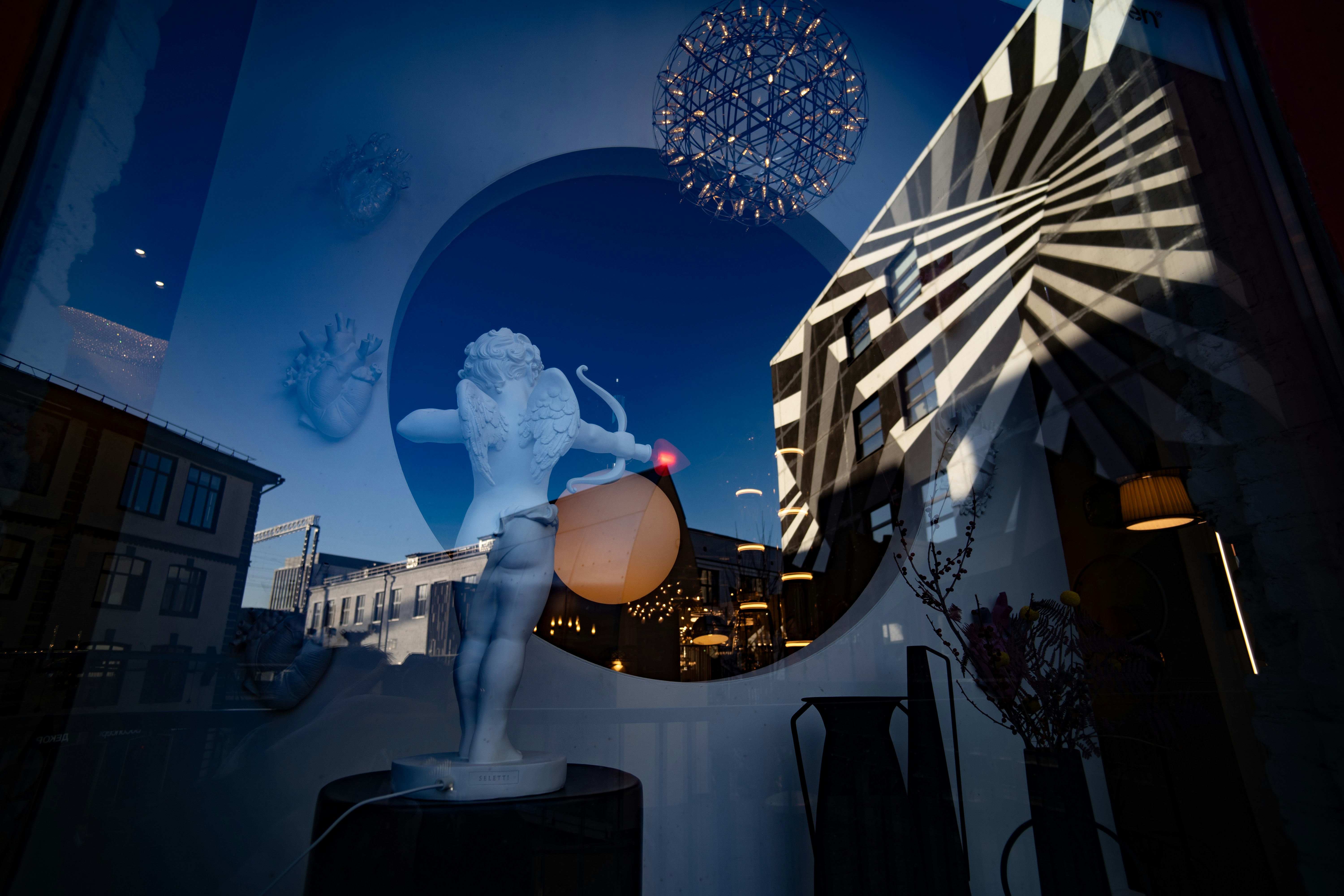 Statue of cupid with building reflections in window.