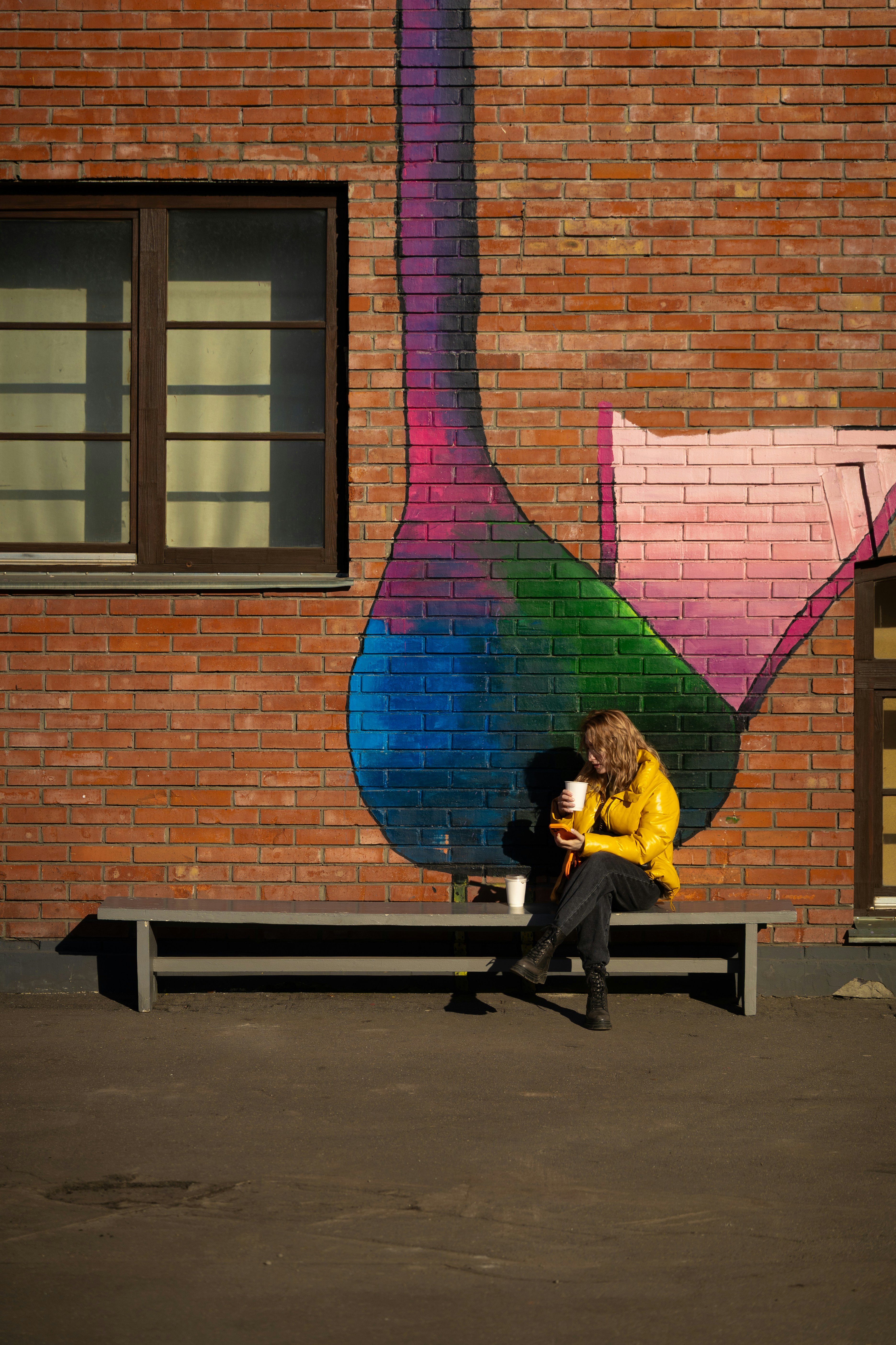Woman in yellow jacket sitting on bench by brick wall