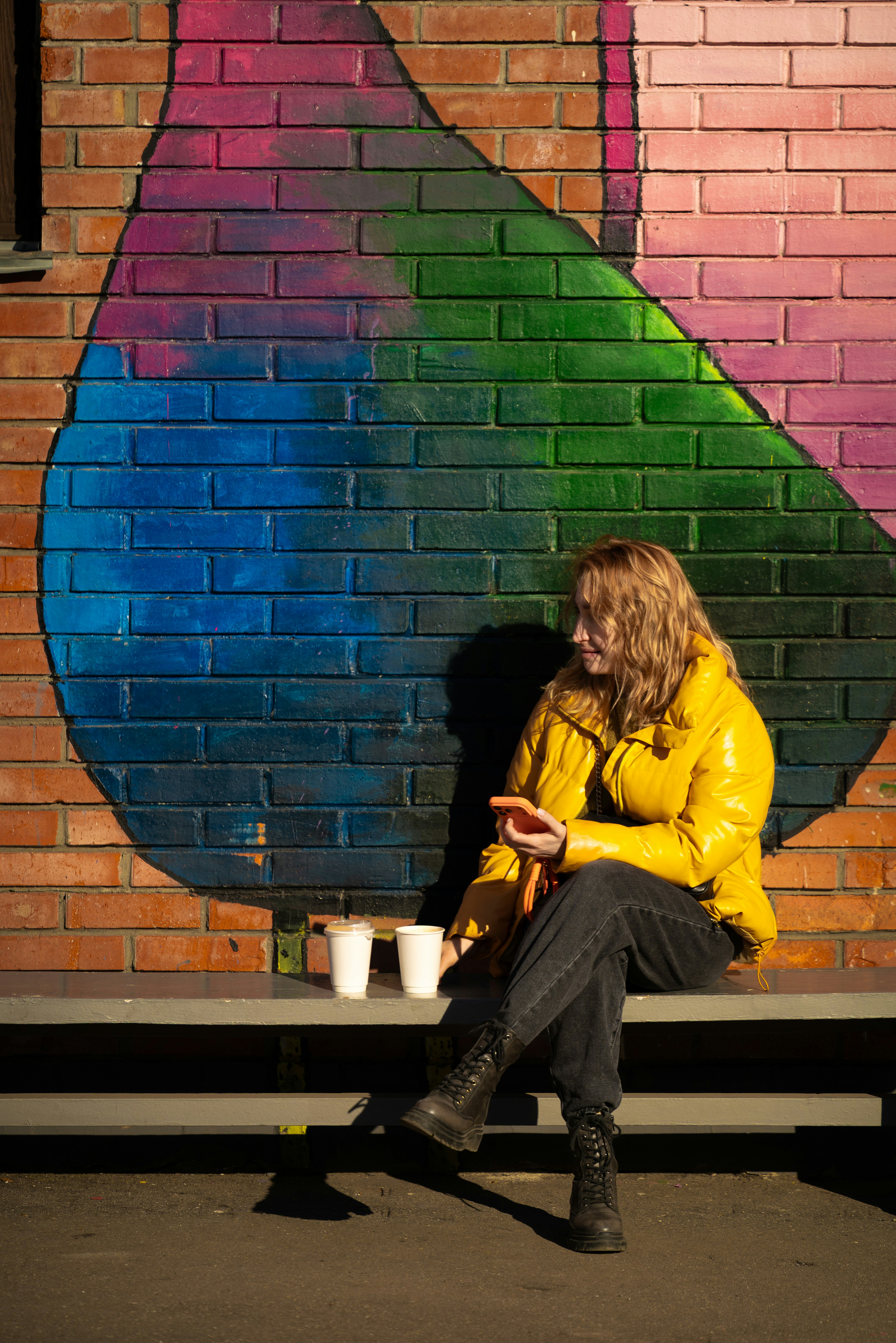 Woman in yellow jacket sits by colorful mural