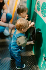 Toddler in overalls plays with a steering wheel.
