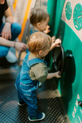 Toddler in overalls plays with a steering wheel.