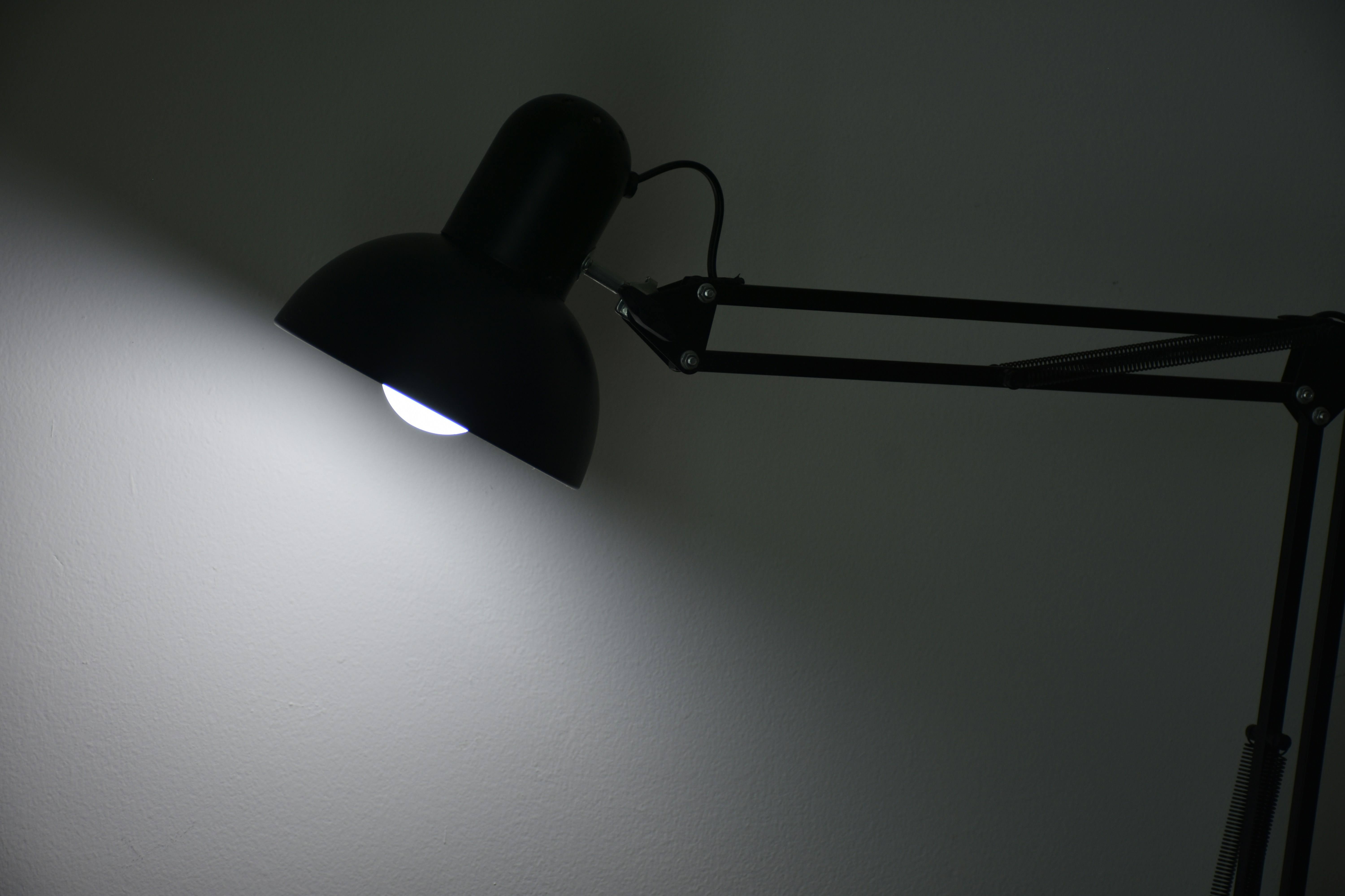 A black desk lamp illuminates a white wall.