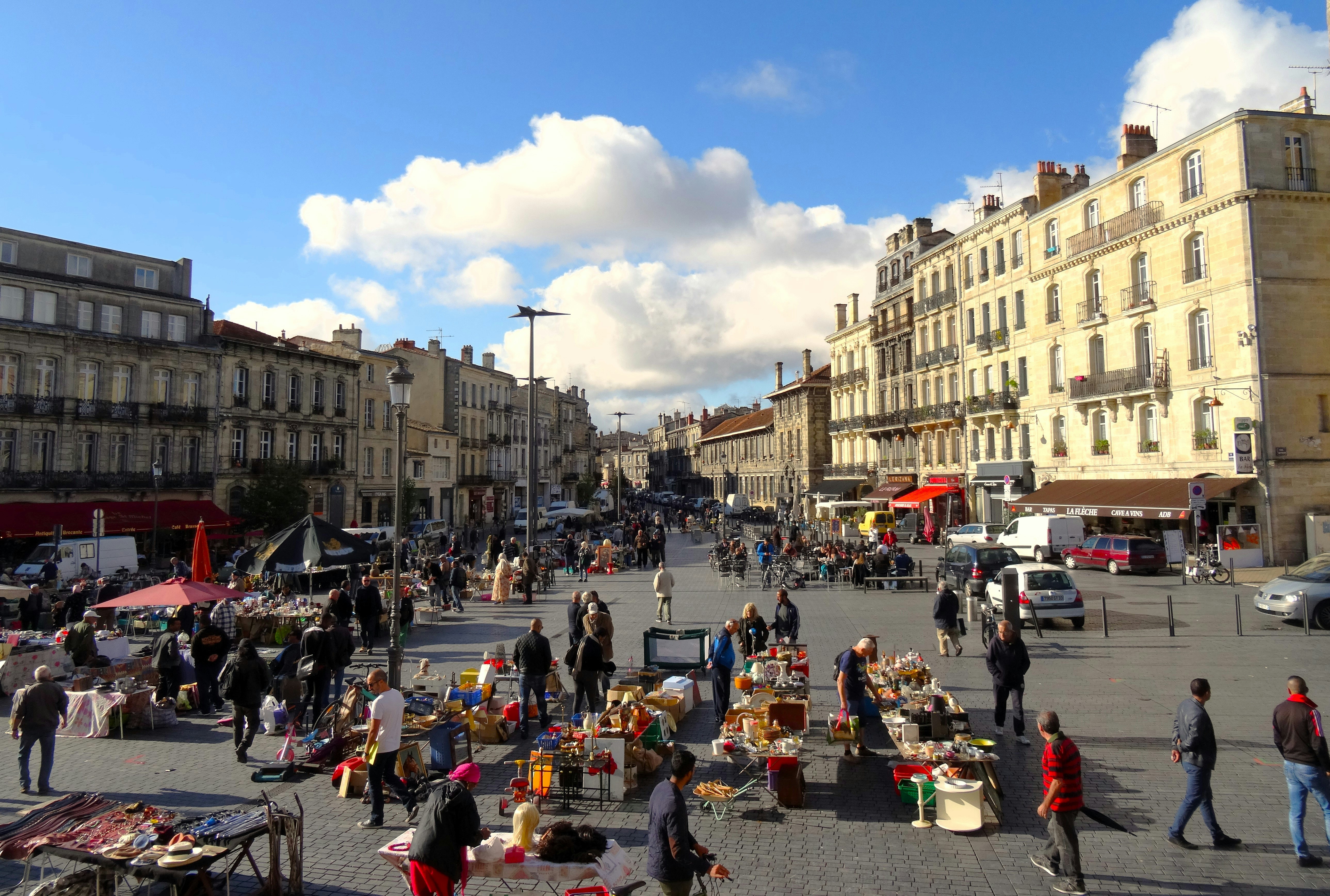 People browsing stalls at an outdoor market with buildings behind.