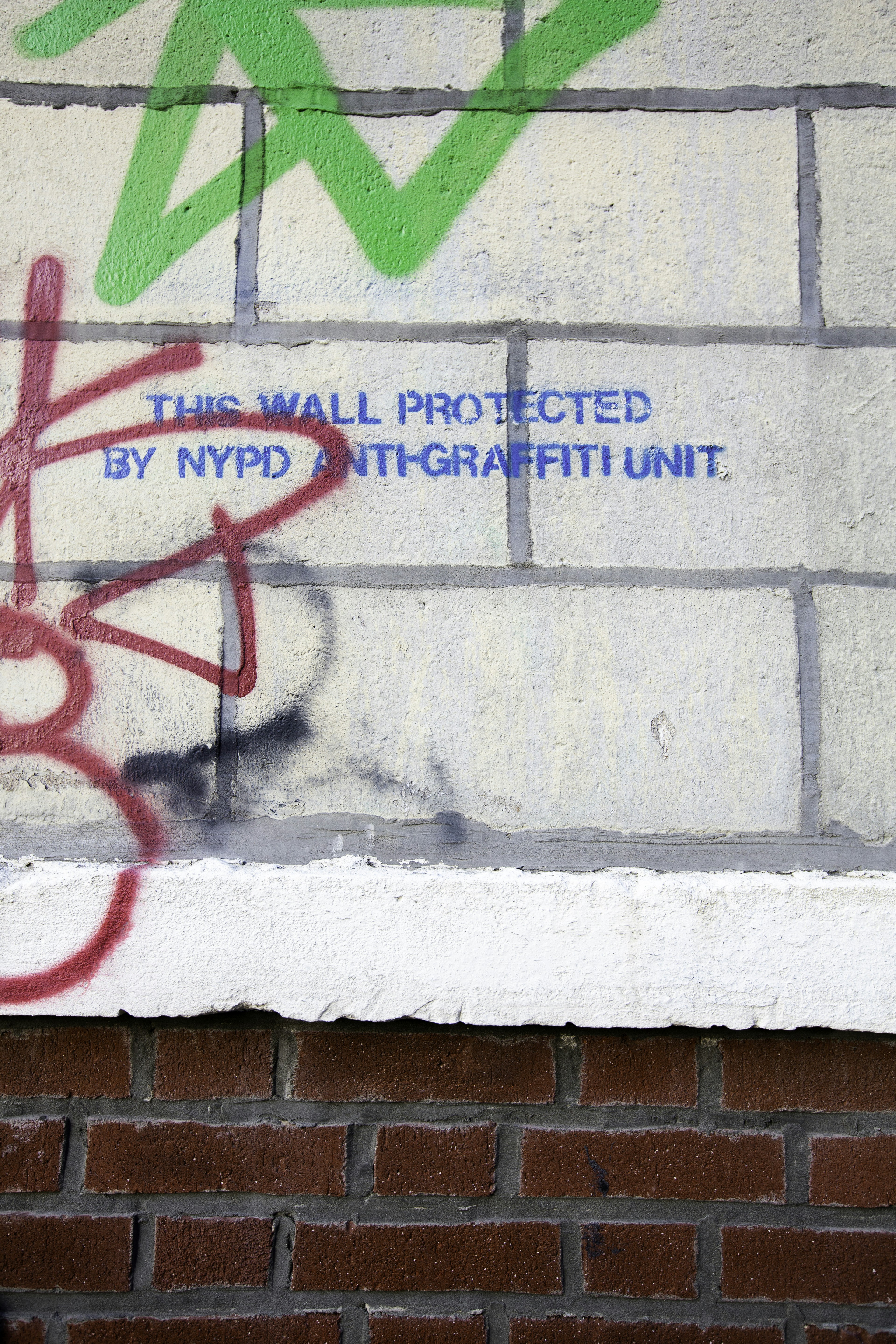 Graffiti su un muro di mattoni con cartello di avvertimento scritto.