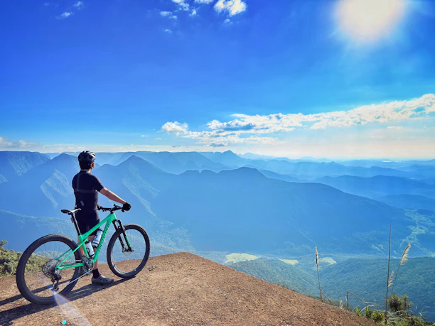 Man with bicycle overlooking mountain range under sunny sky