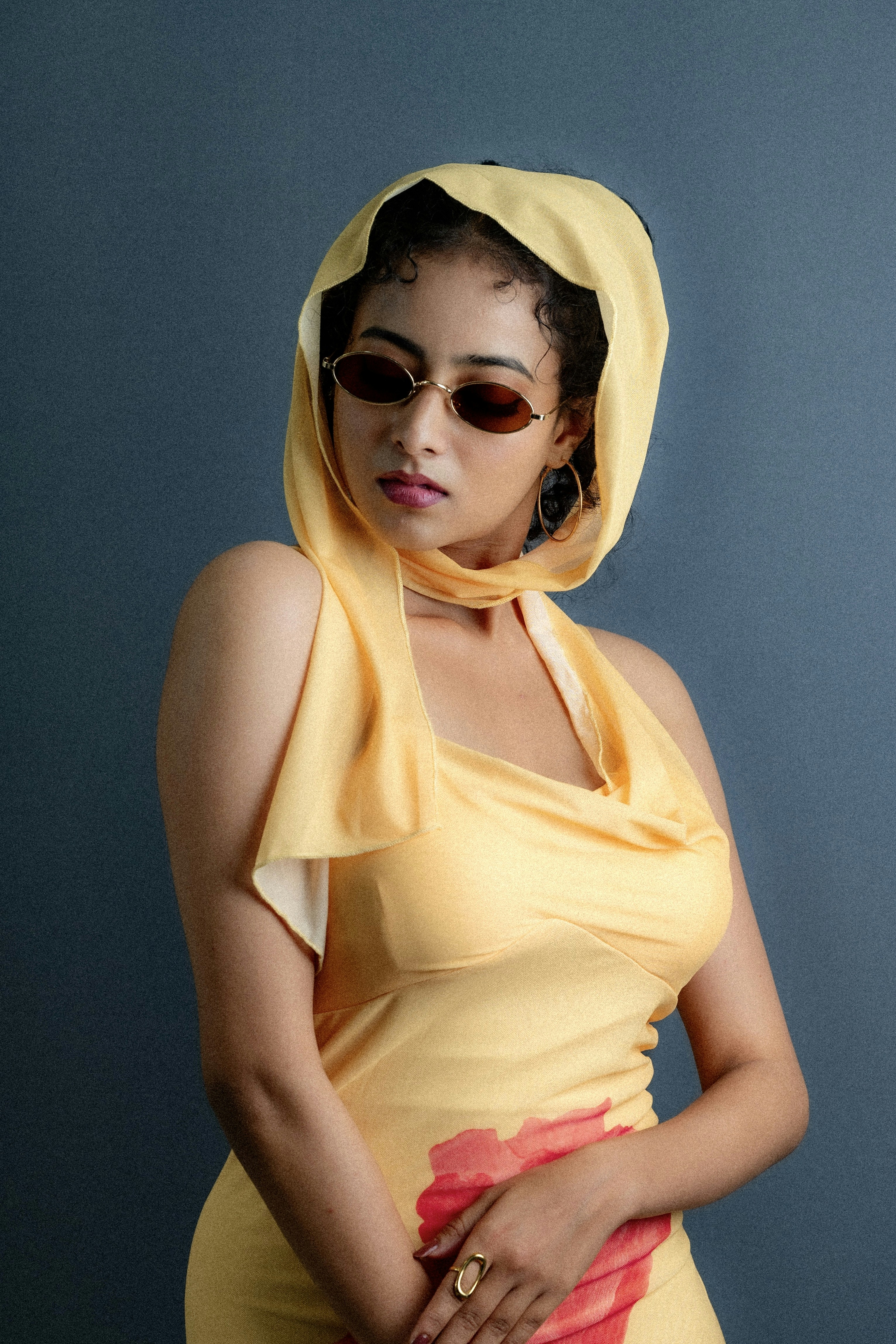 Woman in yellow dress and sunglasses poses against blue background