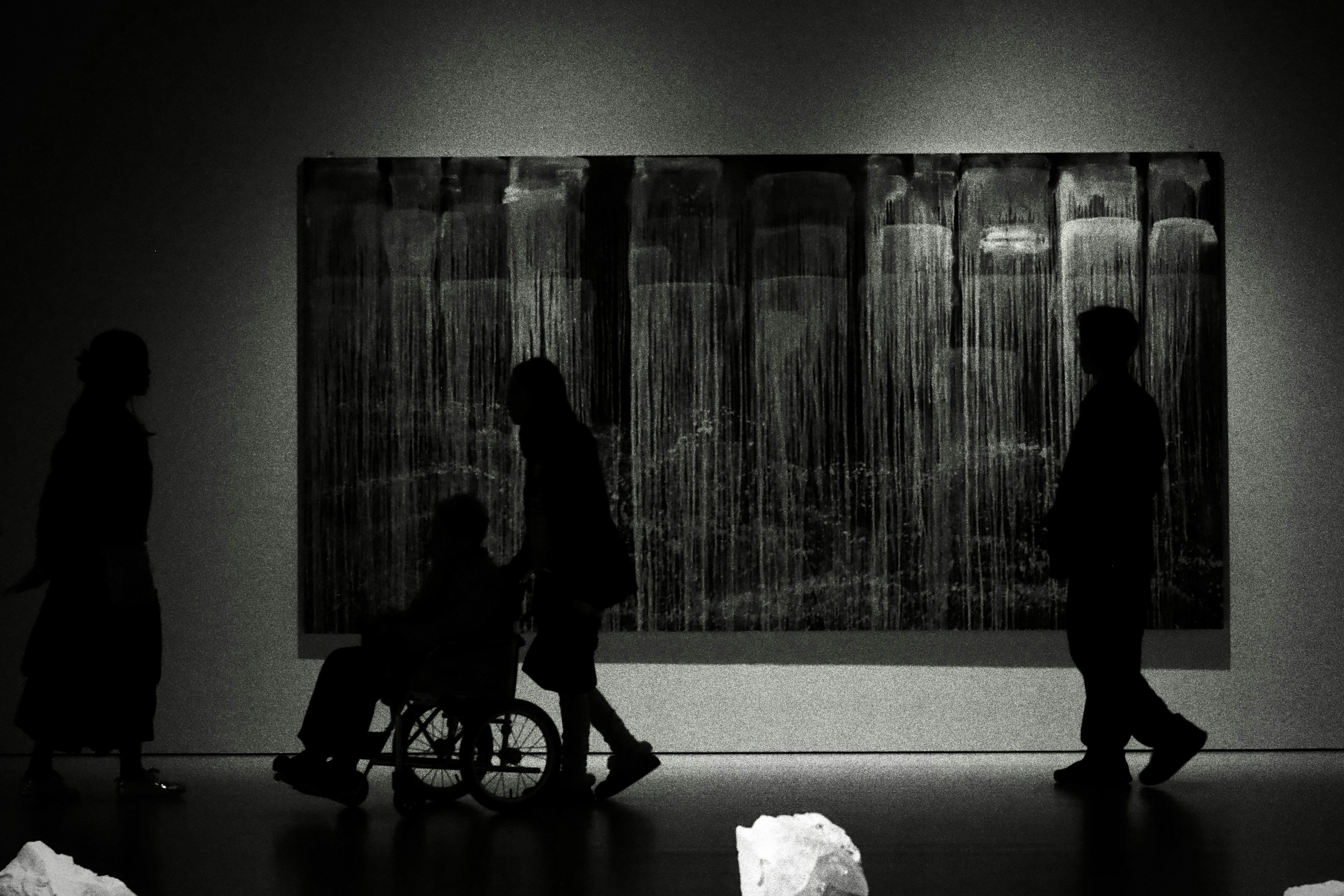 Des silhouettes de personnes observant des œuvres d’art dans une galerie.