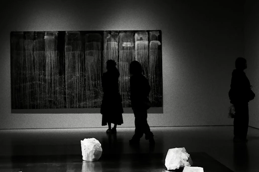 People observing abstract art in a dimly lit gallery.