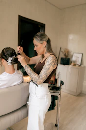 A tattooed hairstylist styles a woman's hair