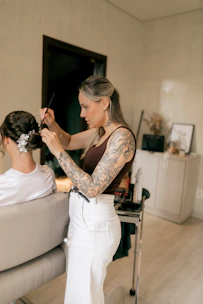 A tattooed hairstylist styles a woman's hair