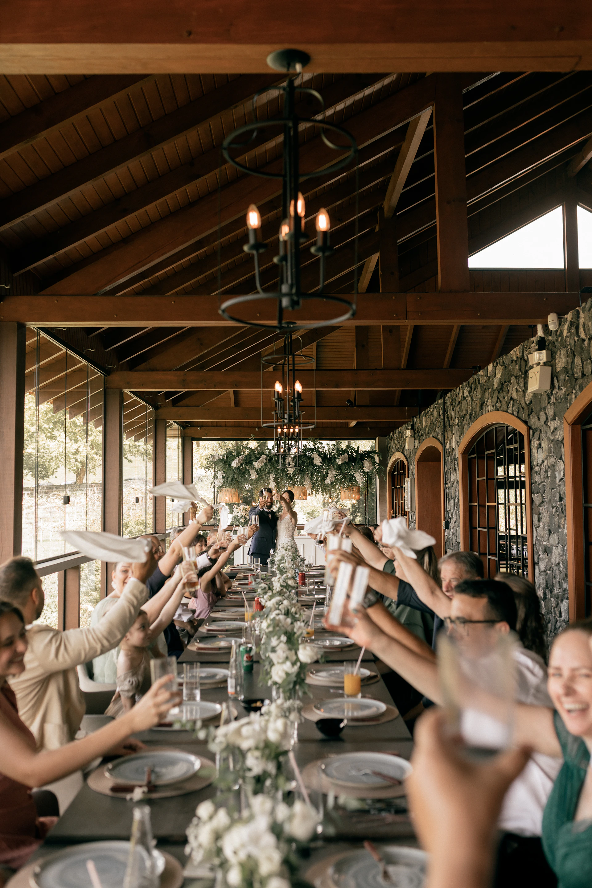 Wedding guests toast the happy couple at a long table.
