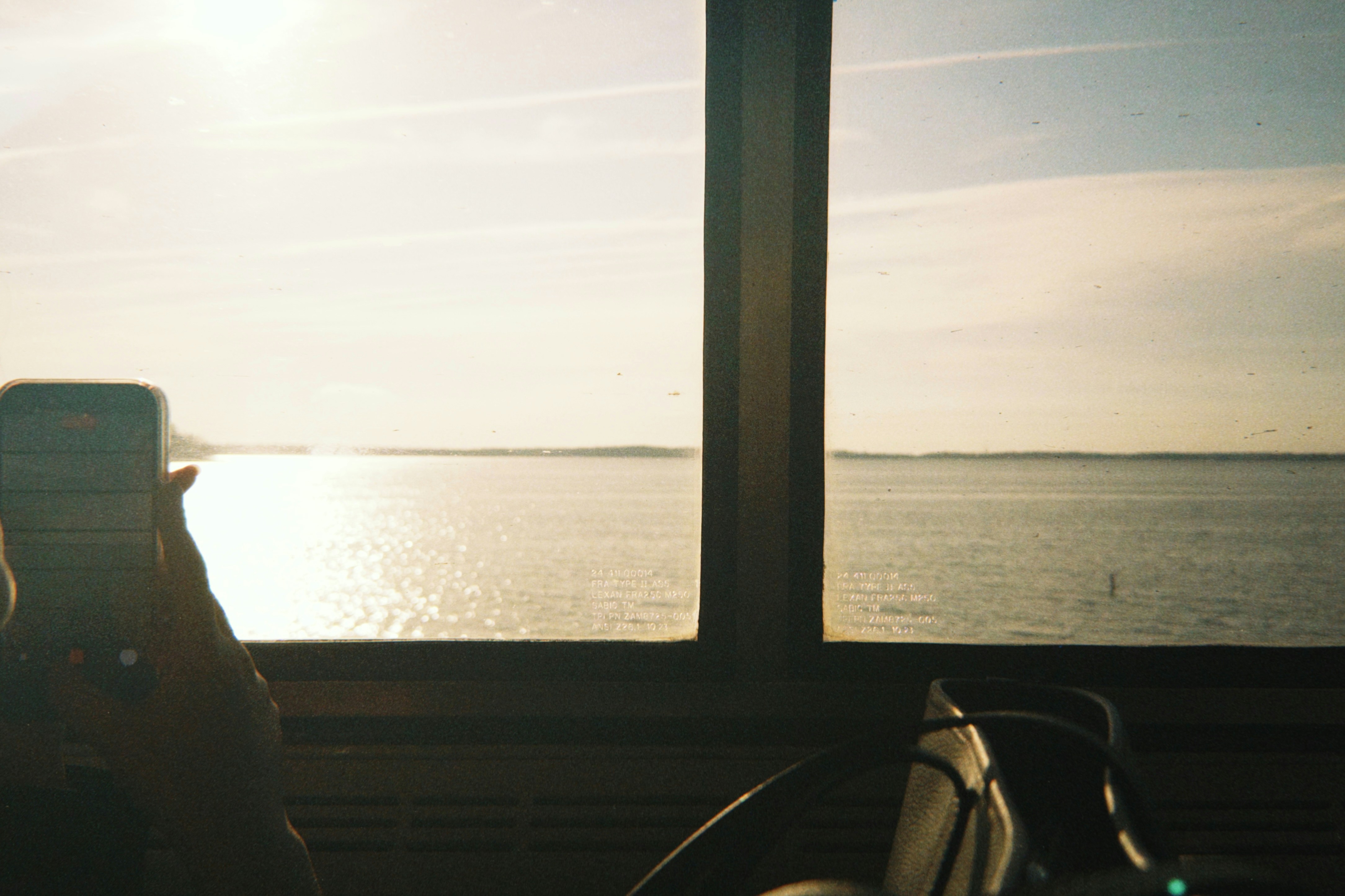 Sunlight reflects on the calm ocean seen through a window.