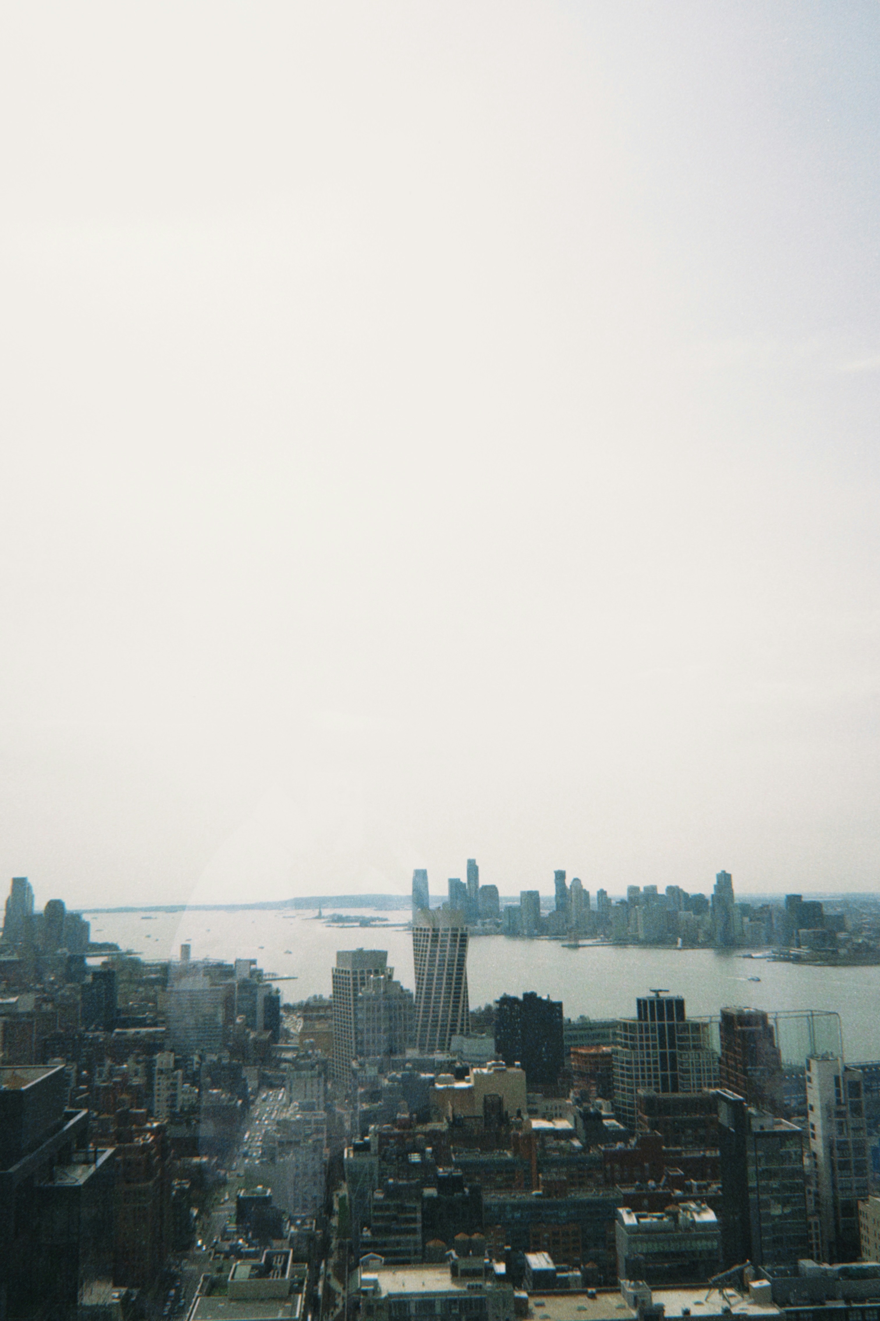 City skyline with river and distant buildings under hazy sky.