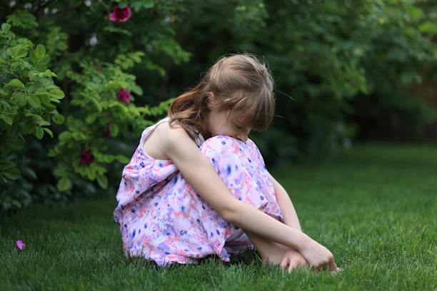 A young girl sits curled up on the grass.
