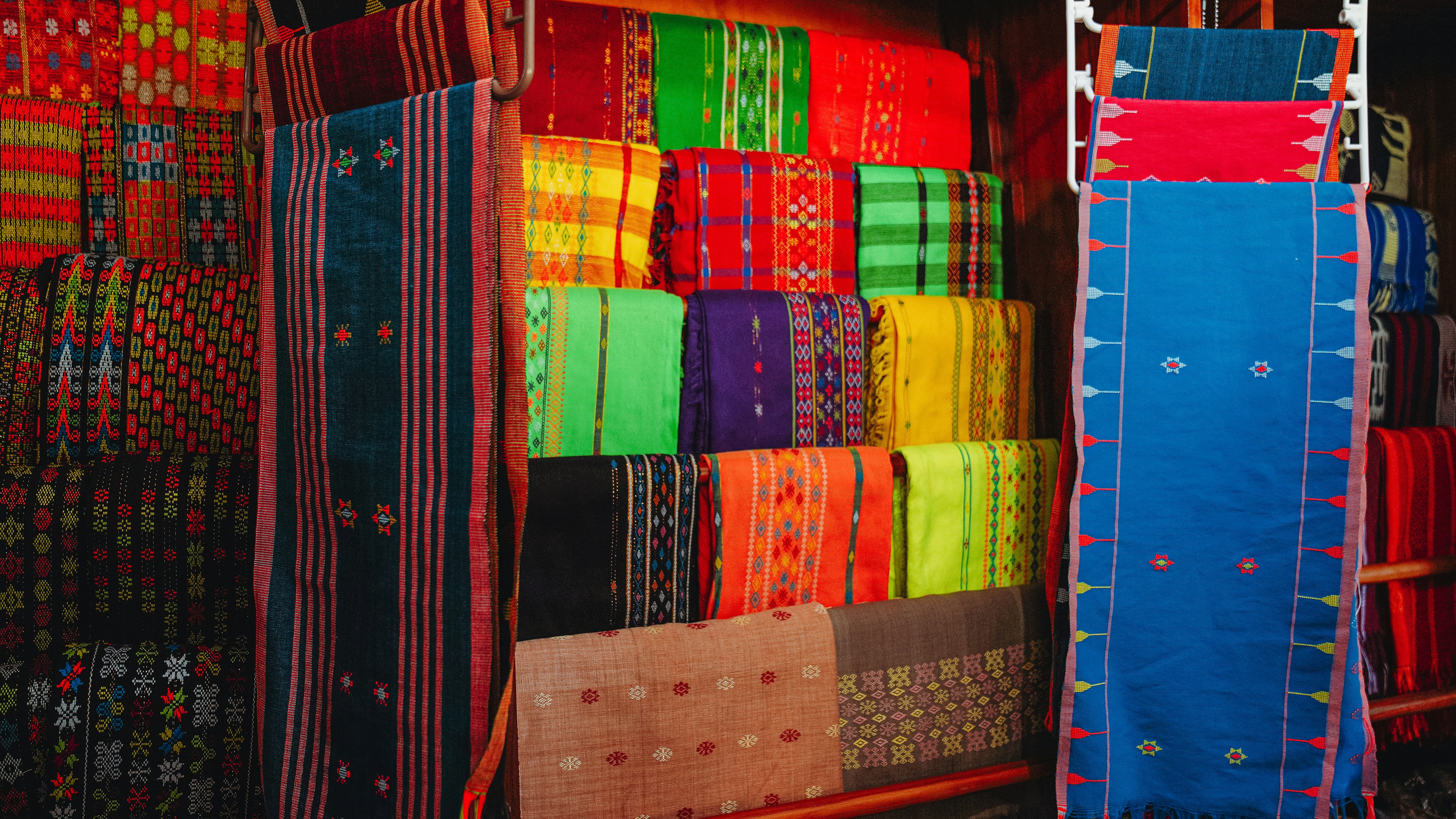 Tekstil tenun warna-warni dipajang di warung pasar