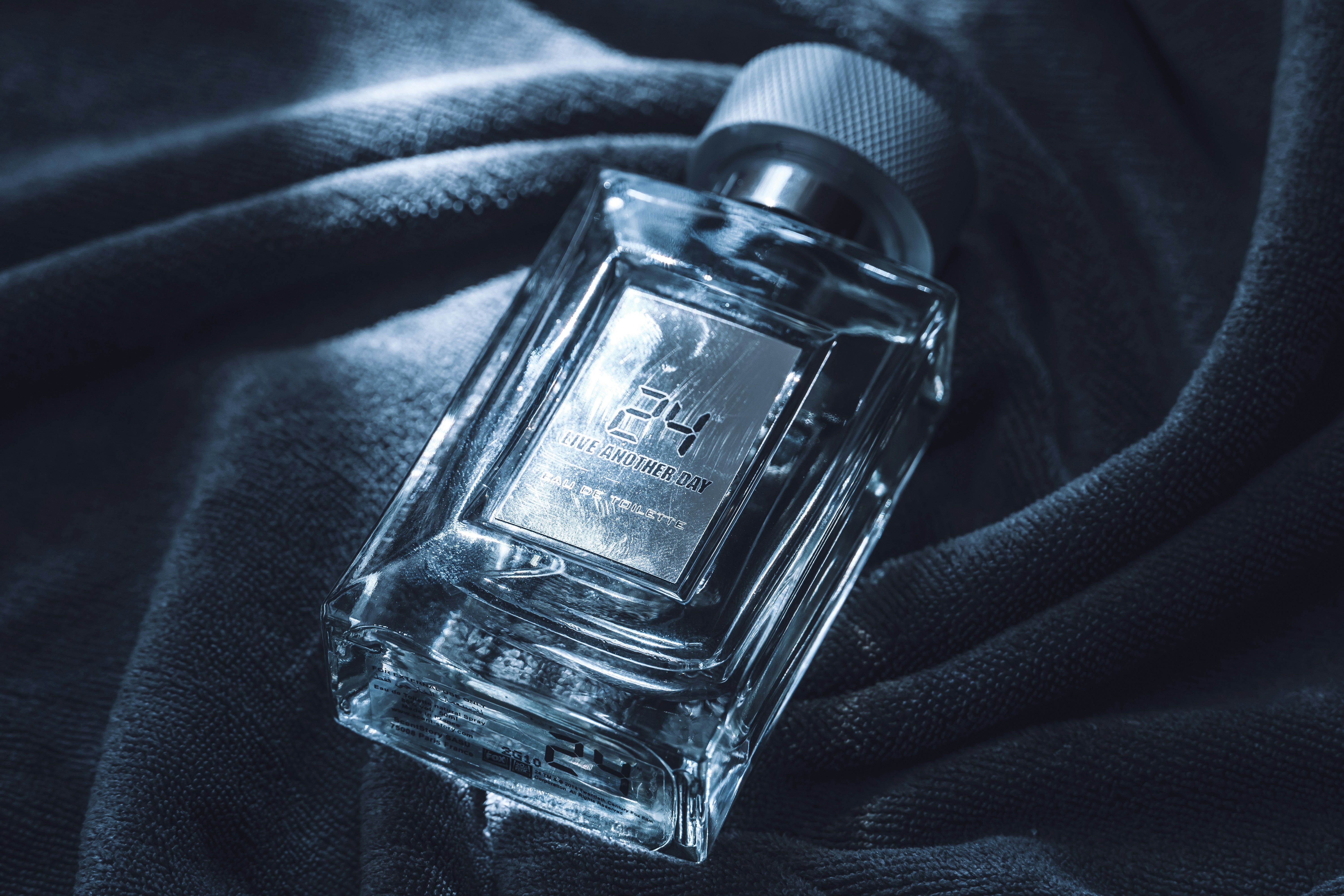 A clear glass perfume bottle on dark fabric