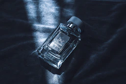 A clear glass perfume bottle with a silver cap