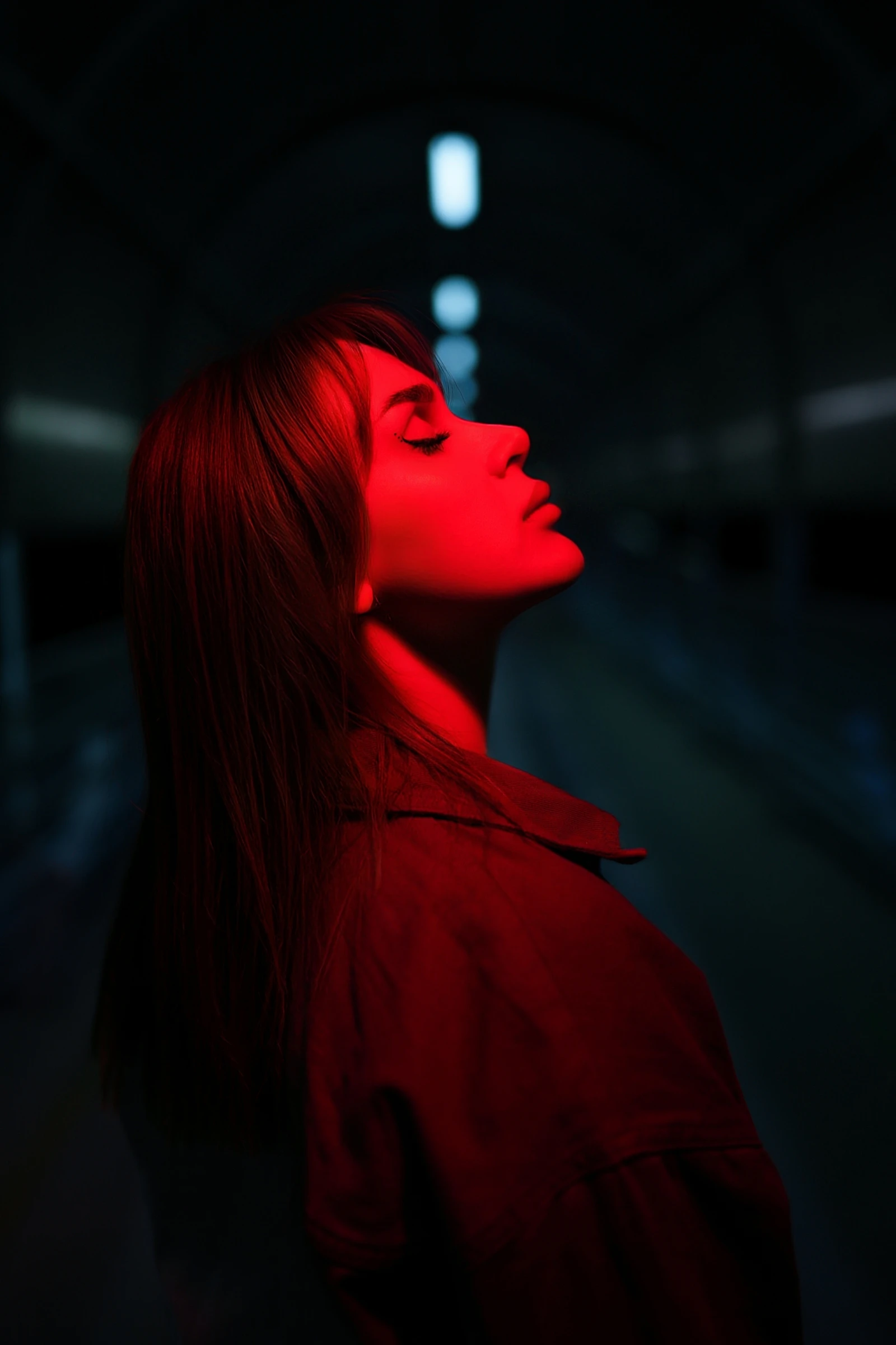 O femeie cu ochii închiși și capul dat pe spate, luminată de o lumină roșie, într-un coridor întunecat