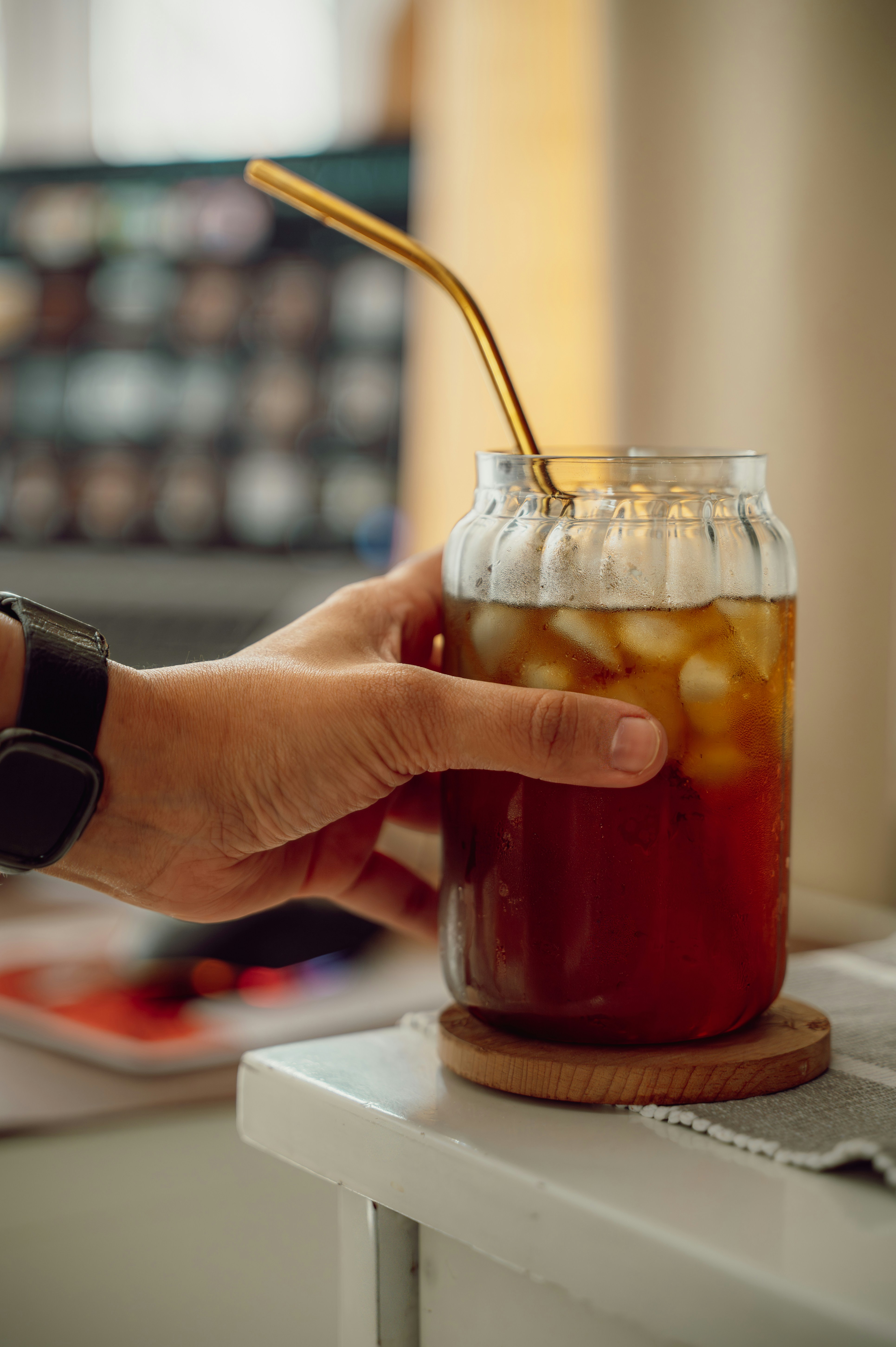 Hand holding a glass of iced tea with a straw.