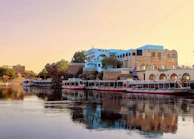 Boats docked on a river with buildings in the background.