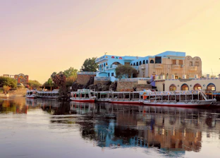 Boats docked on a river with buildings in the background.