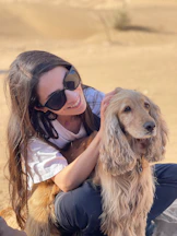 A woman smiles while petting a golden dog outdoors