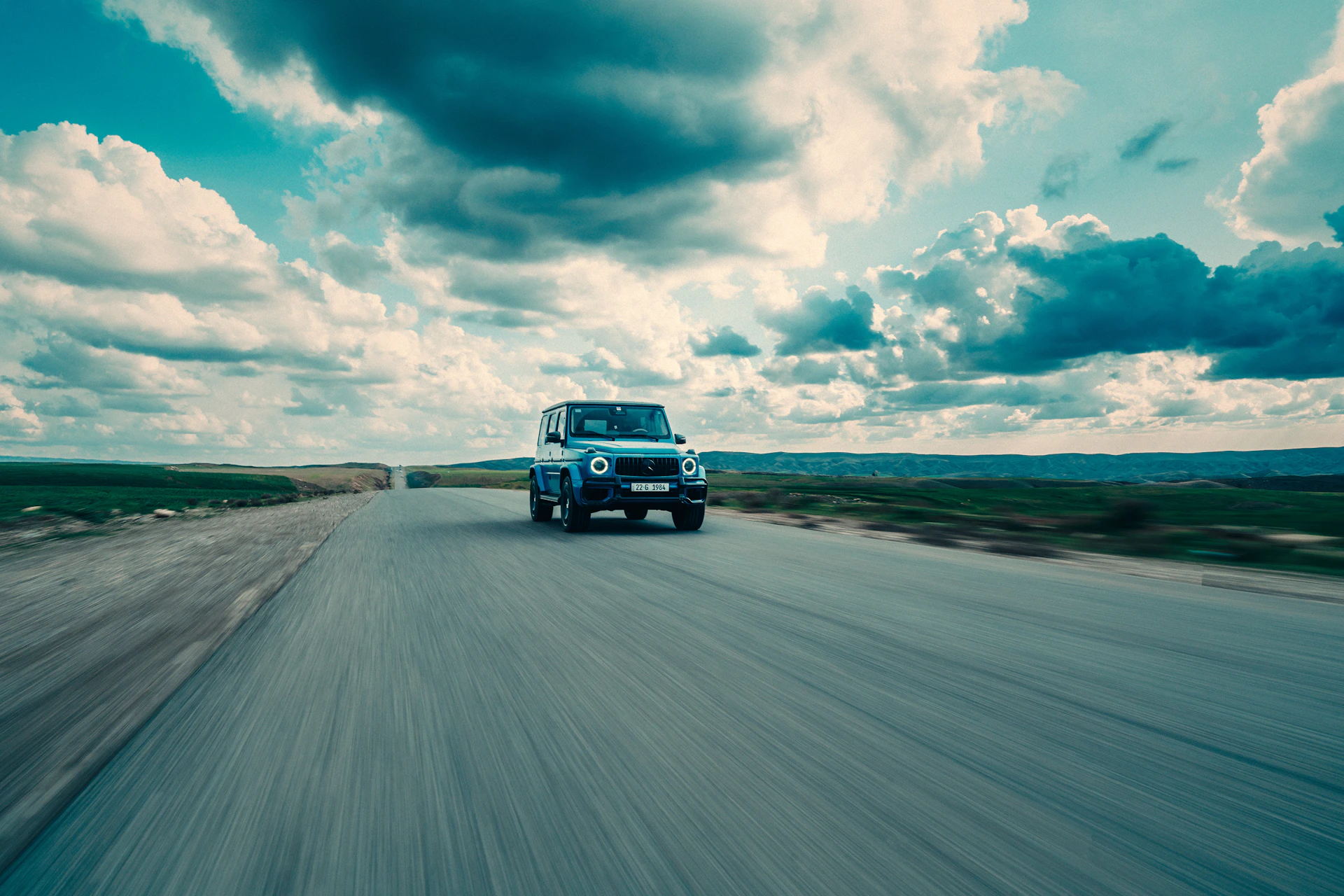 A car drives on a road under a cloudy sky.