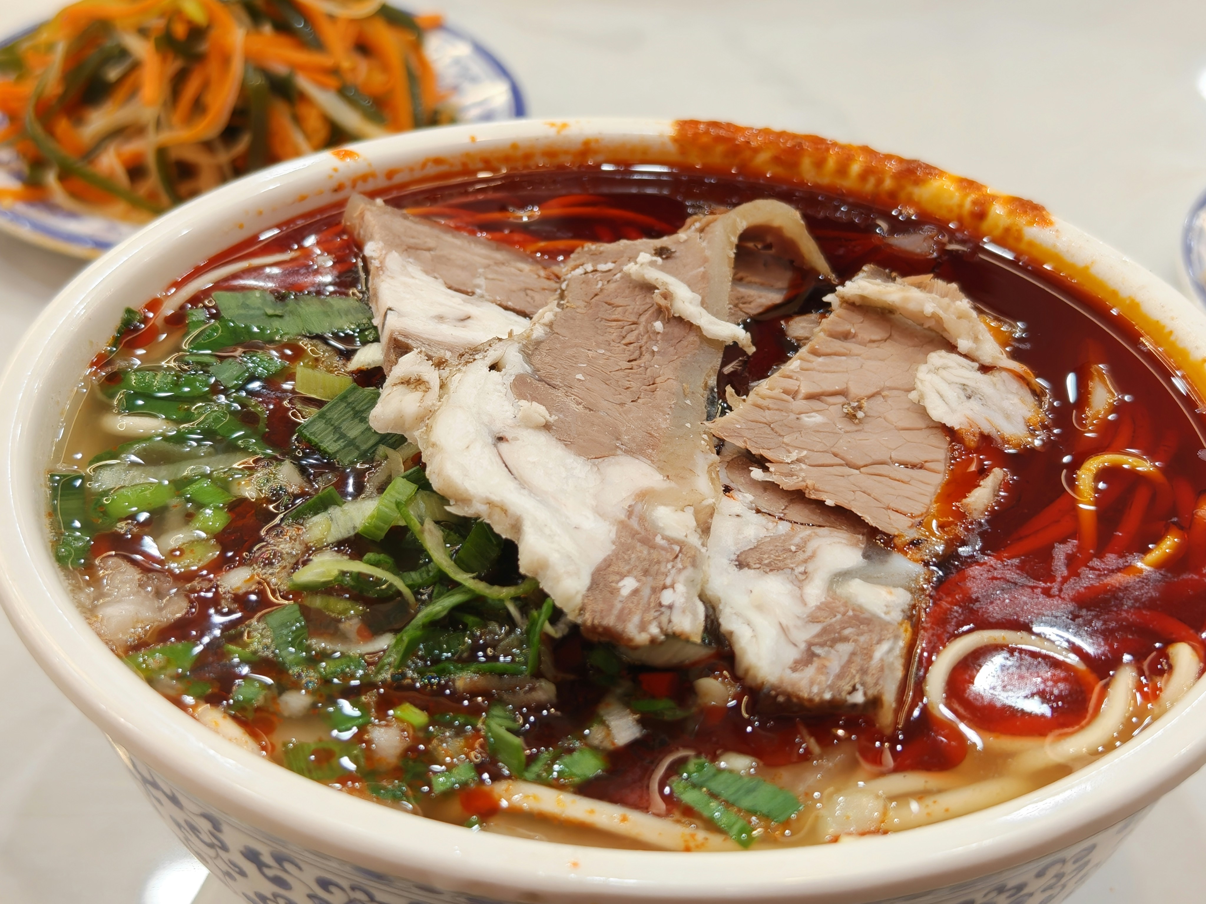 Bowl of noodles with sliced meat and greens.