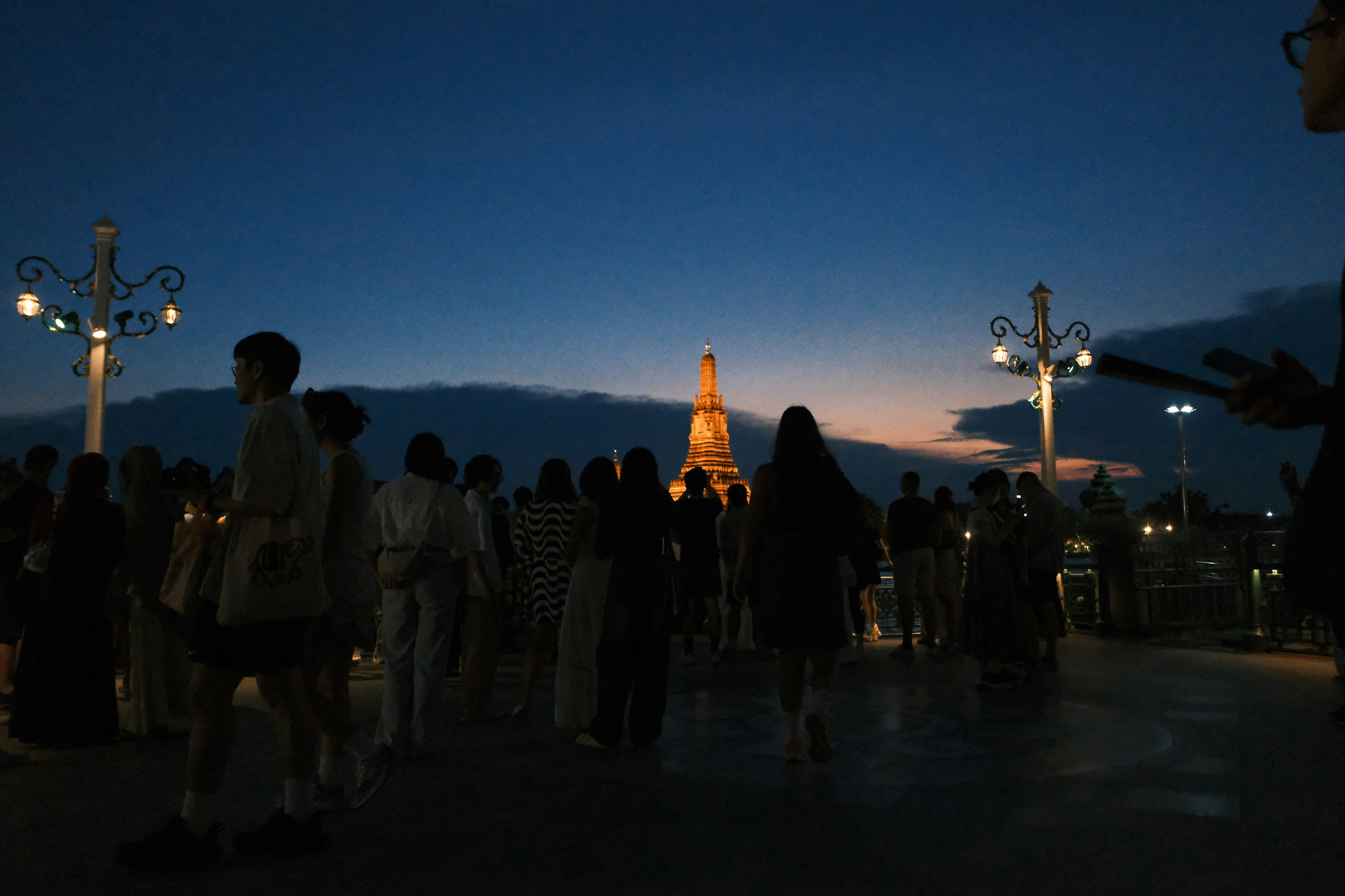 People gather at dusk near a distant illuminated monument.