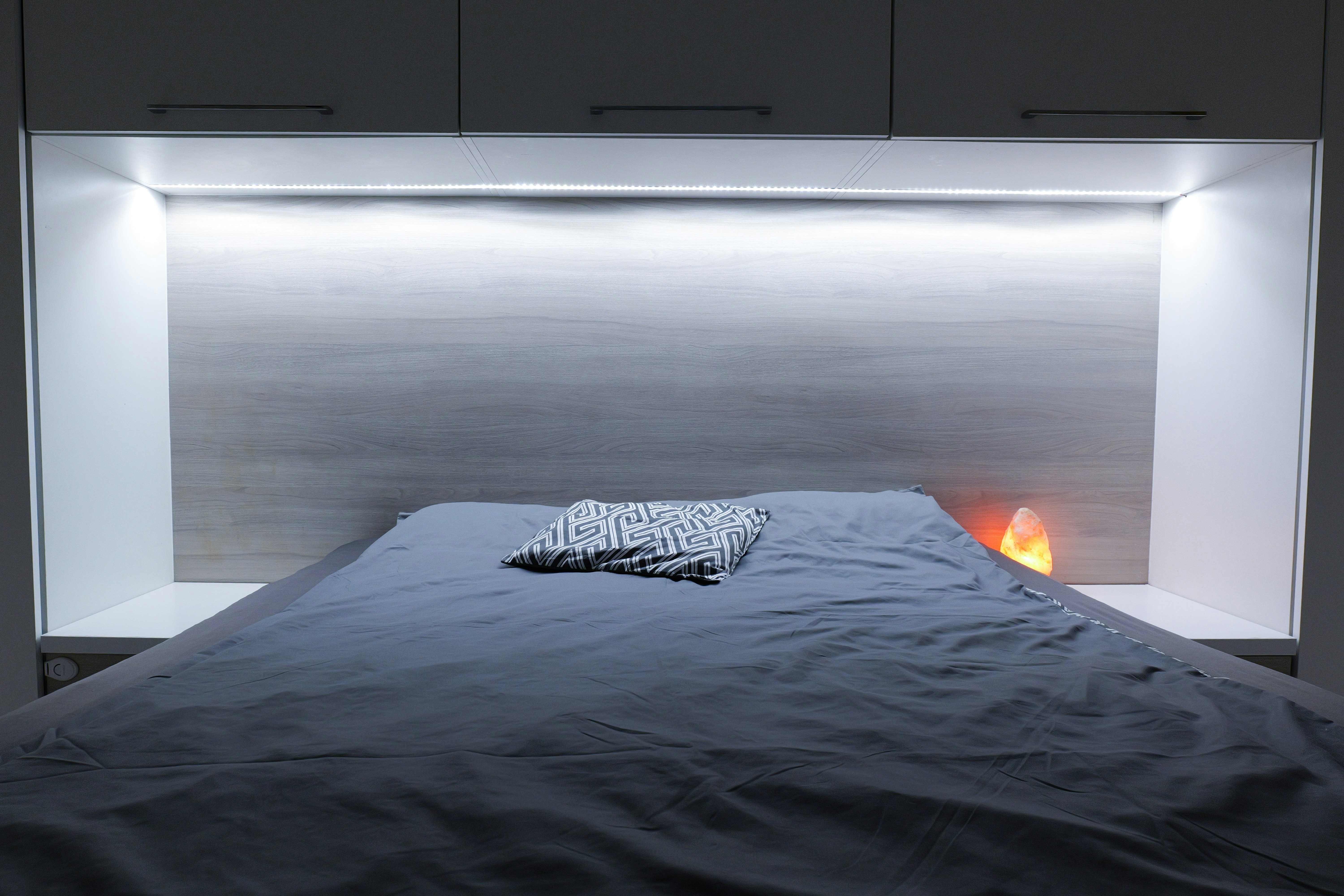 A bed with grey sheets and a patterned pillow.